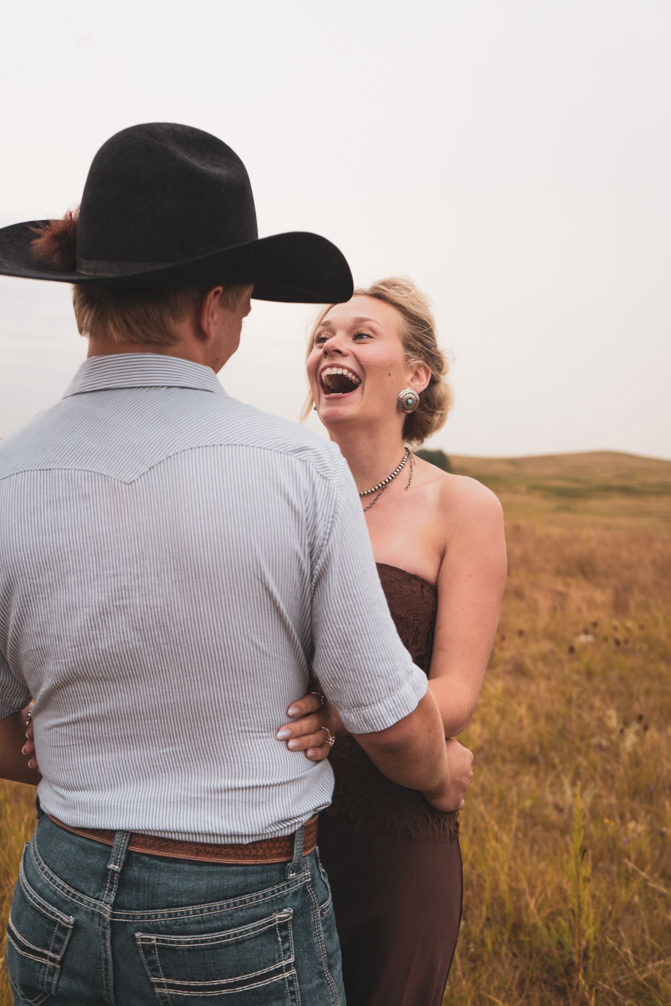 Laughing woman embracing man in black cowboy hat in a wide open golden prairie field.