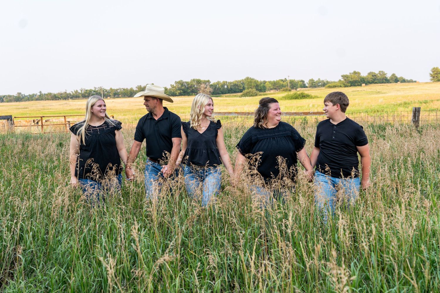 Family of five in black outfits walking hand in hand through tall green field.