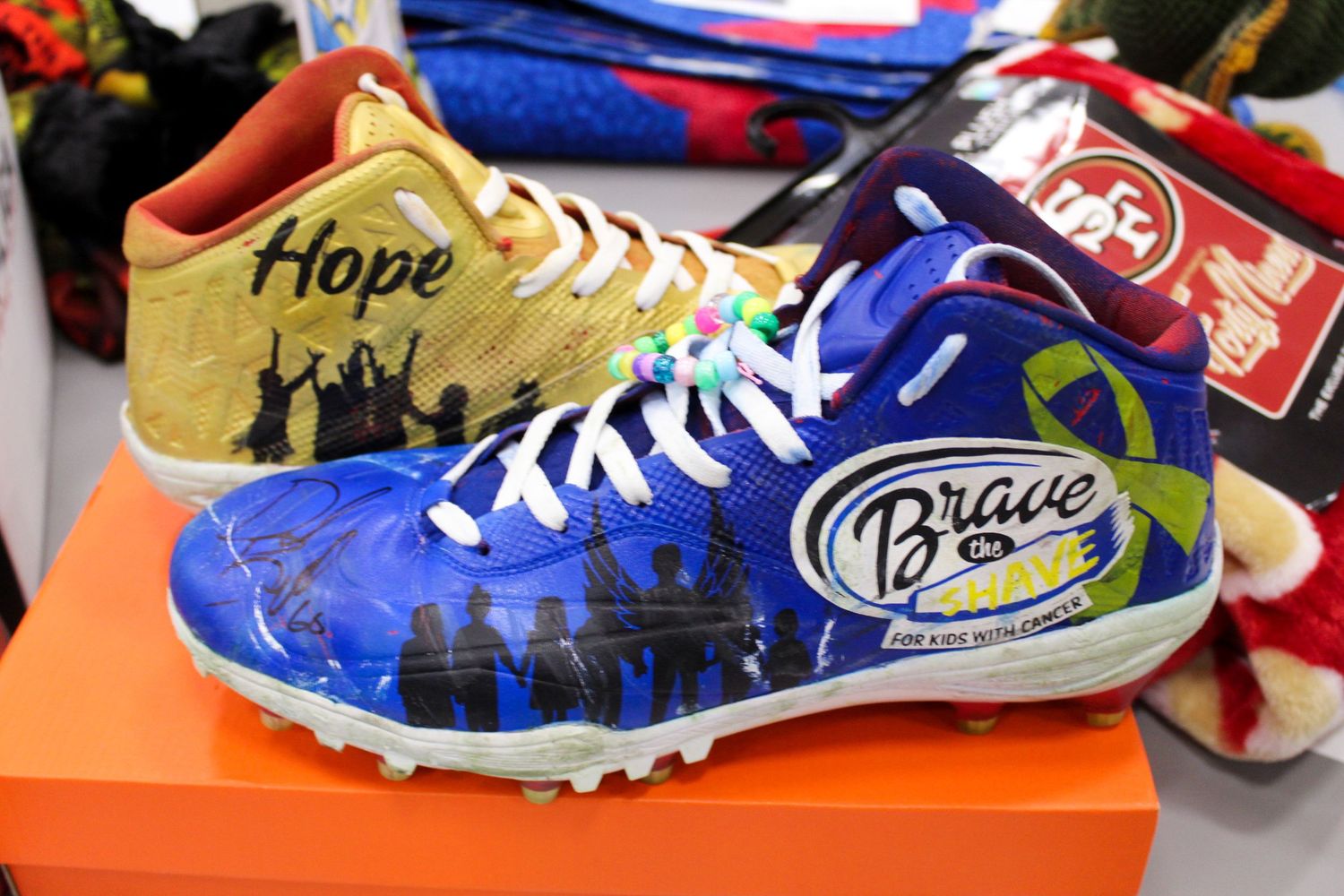 Colorful custom athletic cleat with Hope and Brave the Shave cancer awareness artwork design.