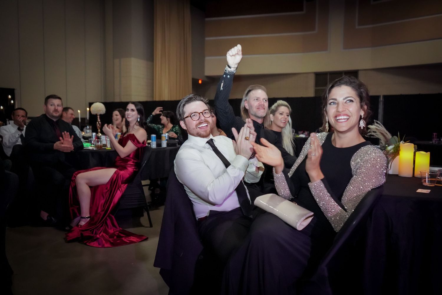 Guests clapping and celebrating at a formal gala event seated at decorated banquet tables.