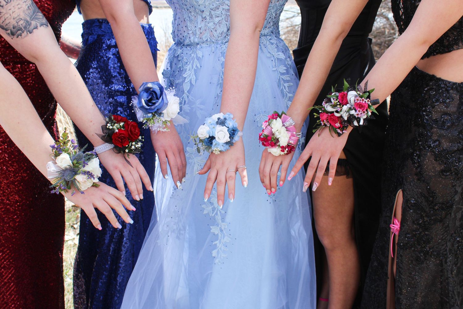 Group of prom girls showing off colorful floral wrist corsages in formal dresses.
