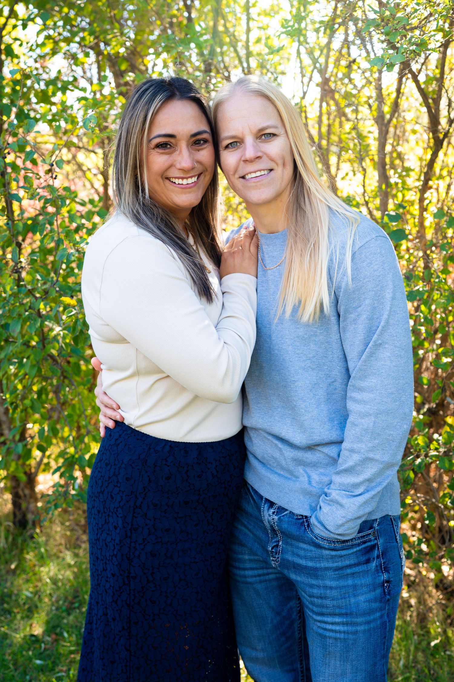 Two happy women hug and smile together in front of lush green foliage.