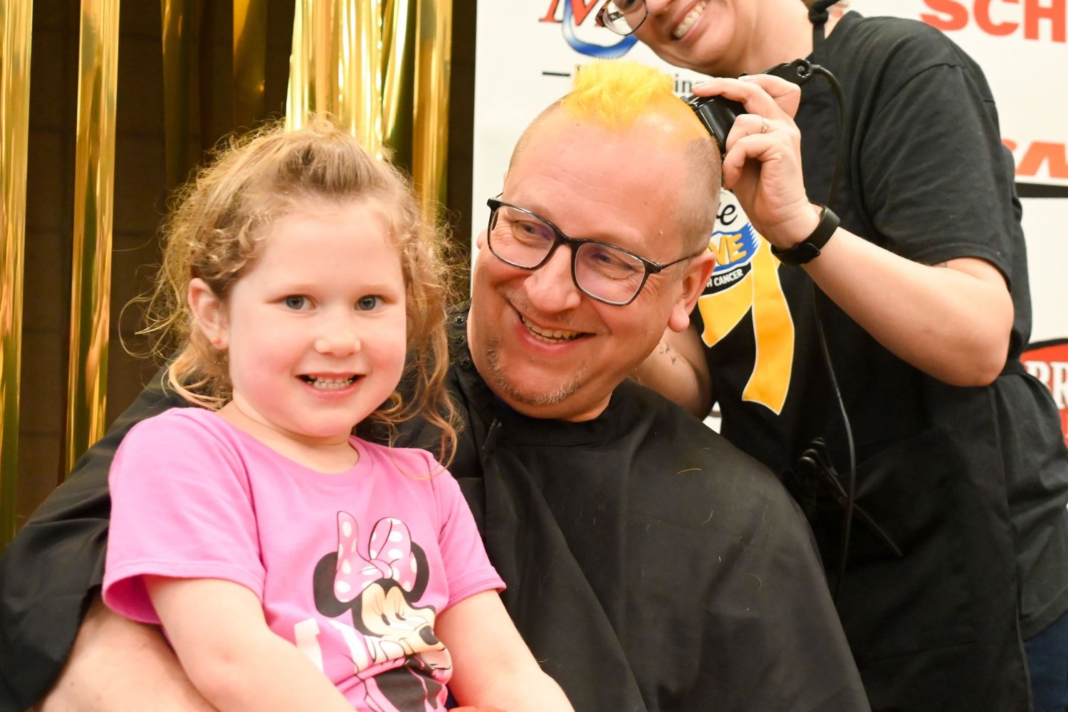 Man with young girl on his lap getting orange hair dyed at a Brave the Shave event.