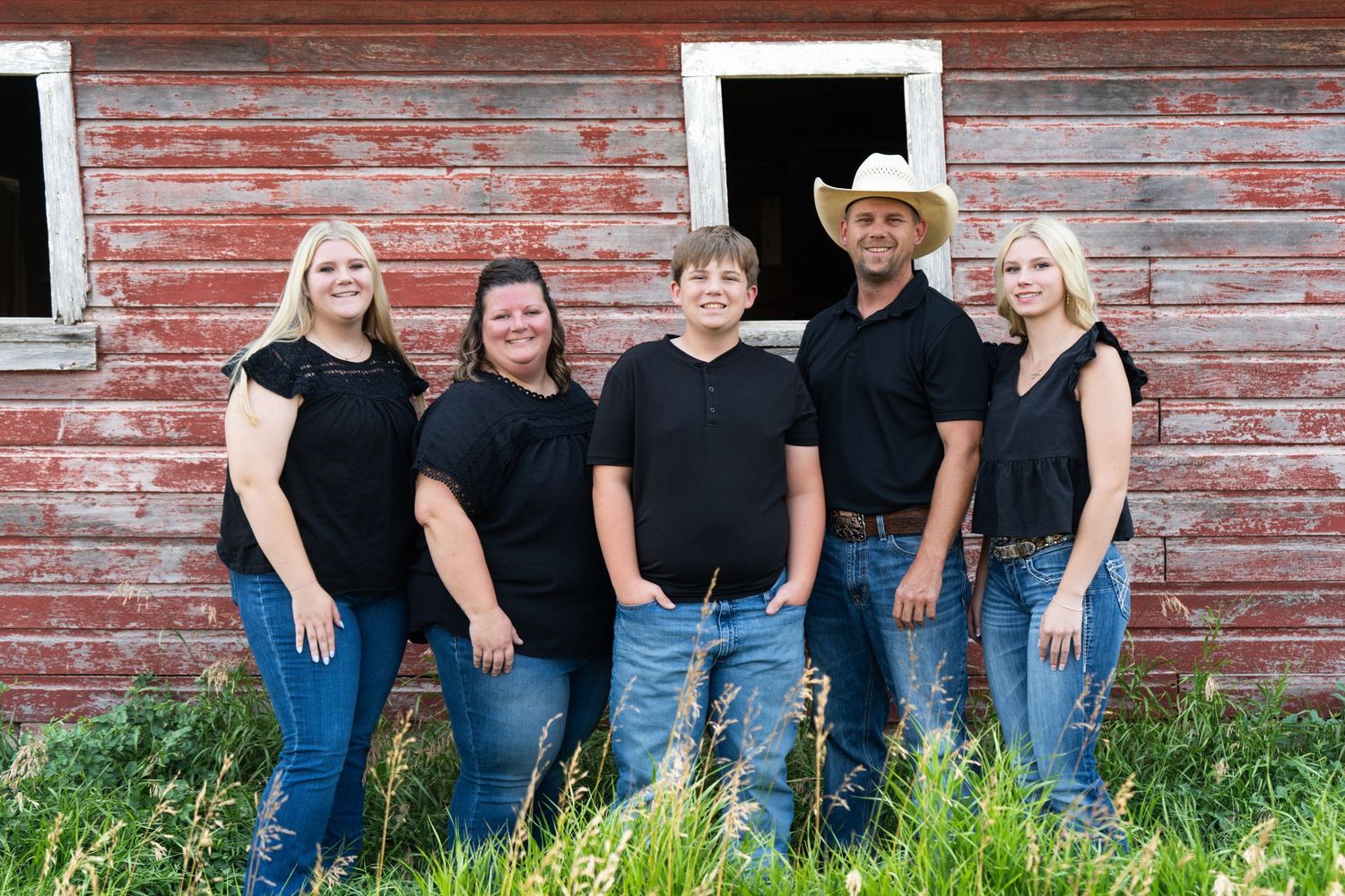 Family of five in matching black outfits pose together in front of a weathered red barn.