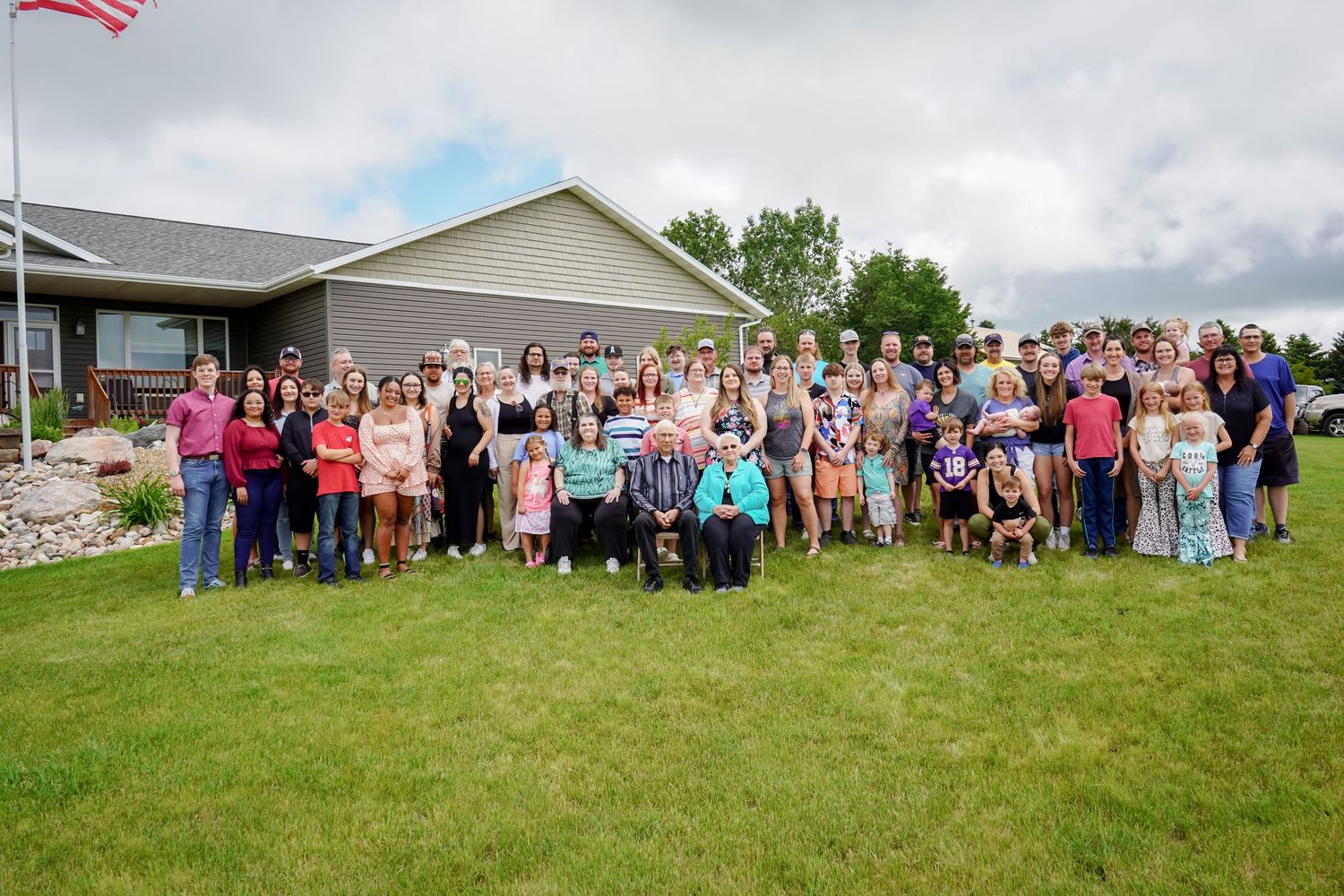 Large group of people posing together outdoors on green lawn in front of a residential home.