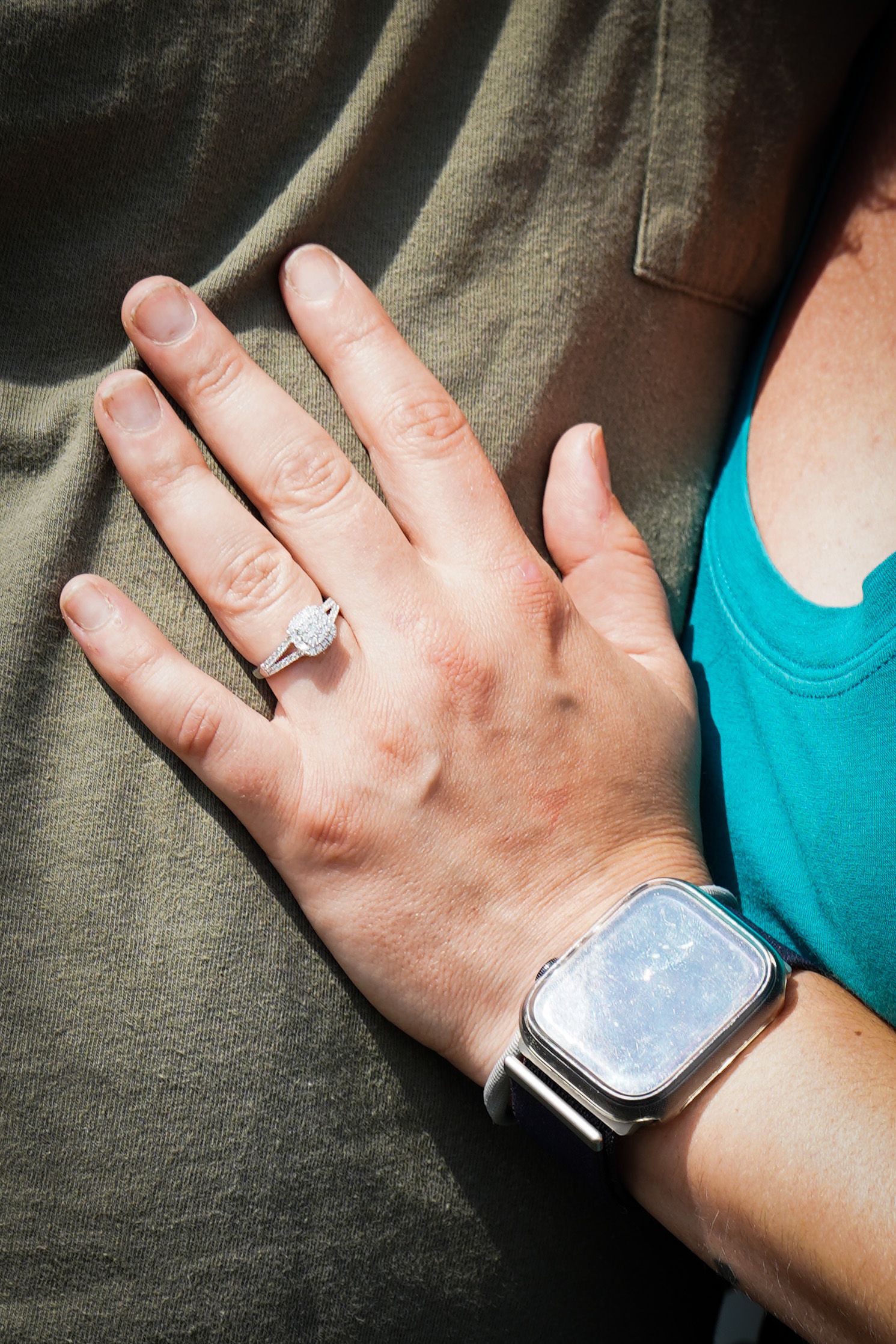 Close-up of engagement ring on woman's hand resting on man's olive shirt.