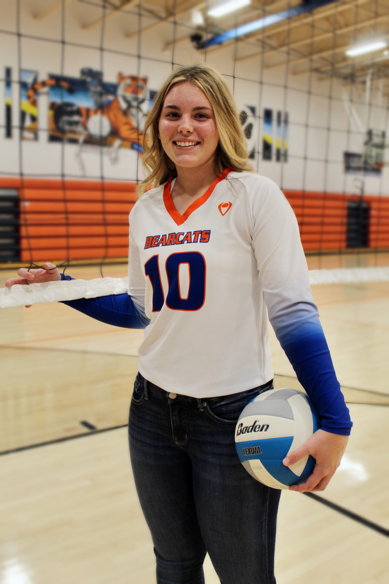 A smiling female volleyball player in a Bearcats number 10 jersey holds a volleyball in a gymnasium.