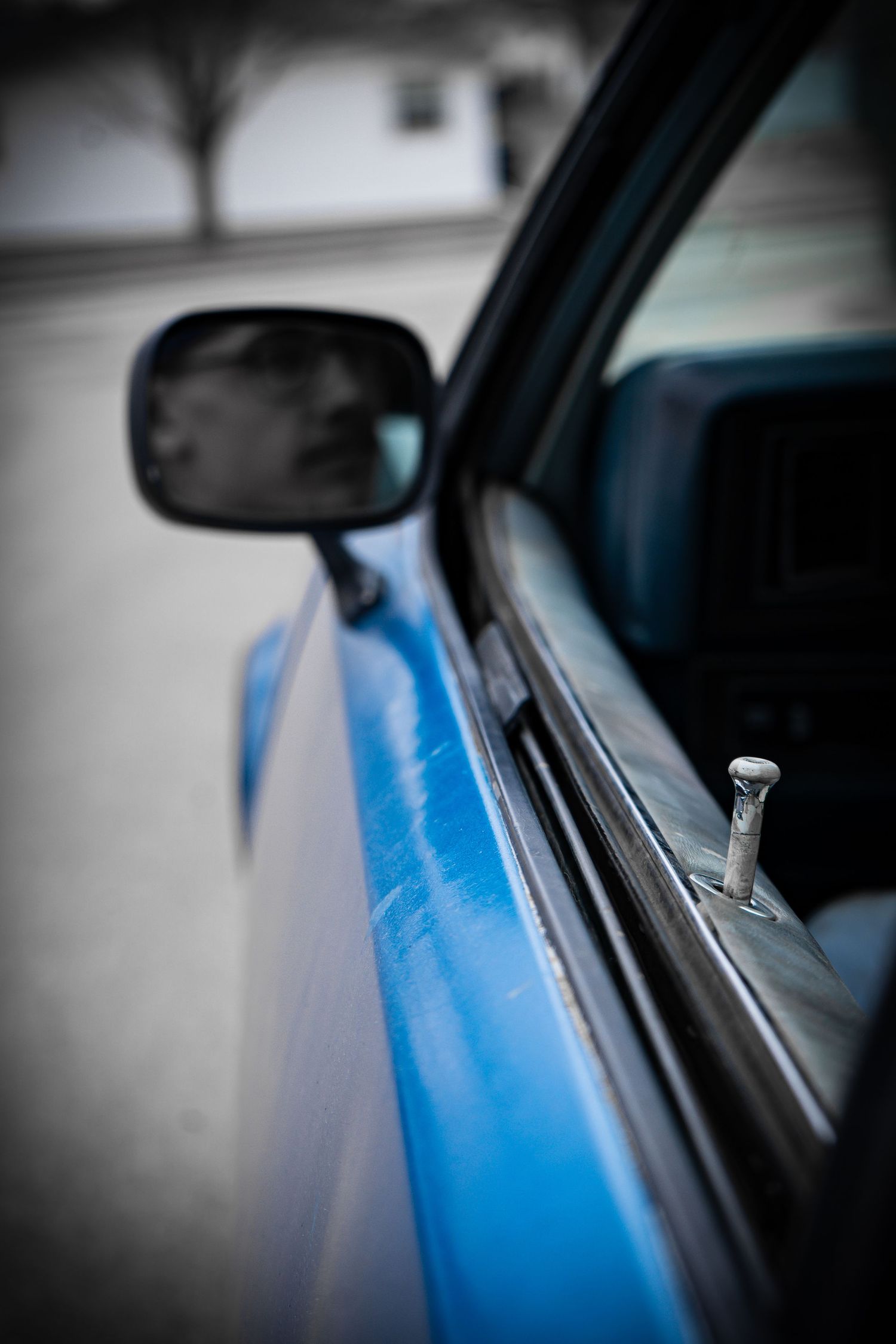 Close-up detail of vintage blue truck door with chrome vent window latch and mirror.