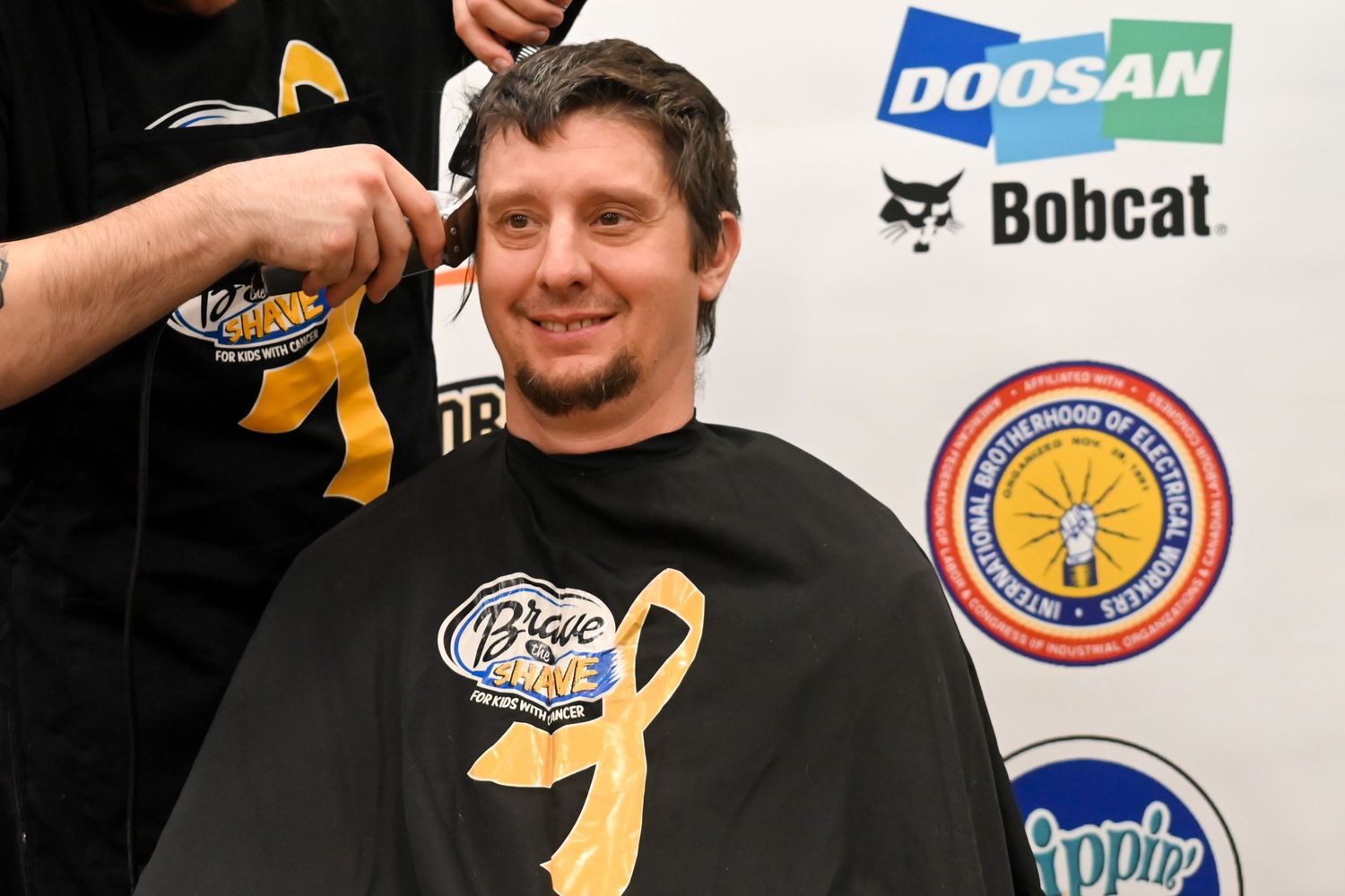 Smiling man getting his head shaved at a Brave the Shave cancer charity fundraising event.