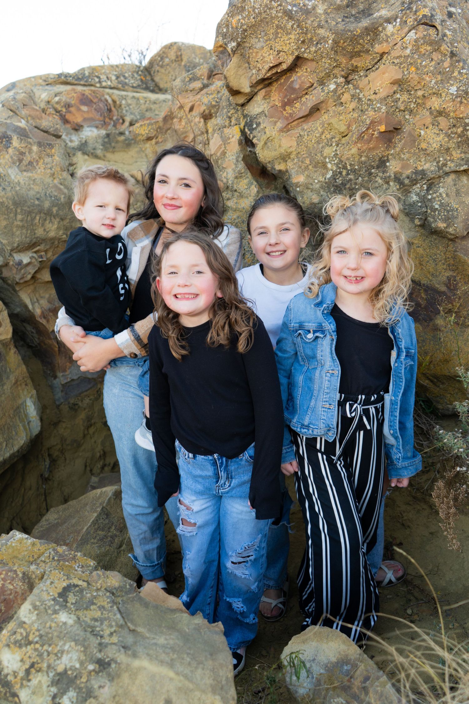 Mother with four young children smiling together among large rocks outdoors.