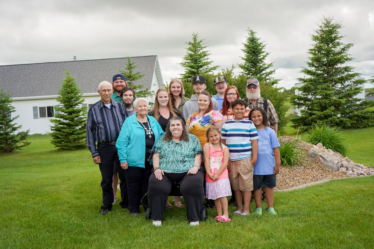 Large extended family group portrait taken outdoors on a green lawn near evergreen trees.