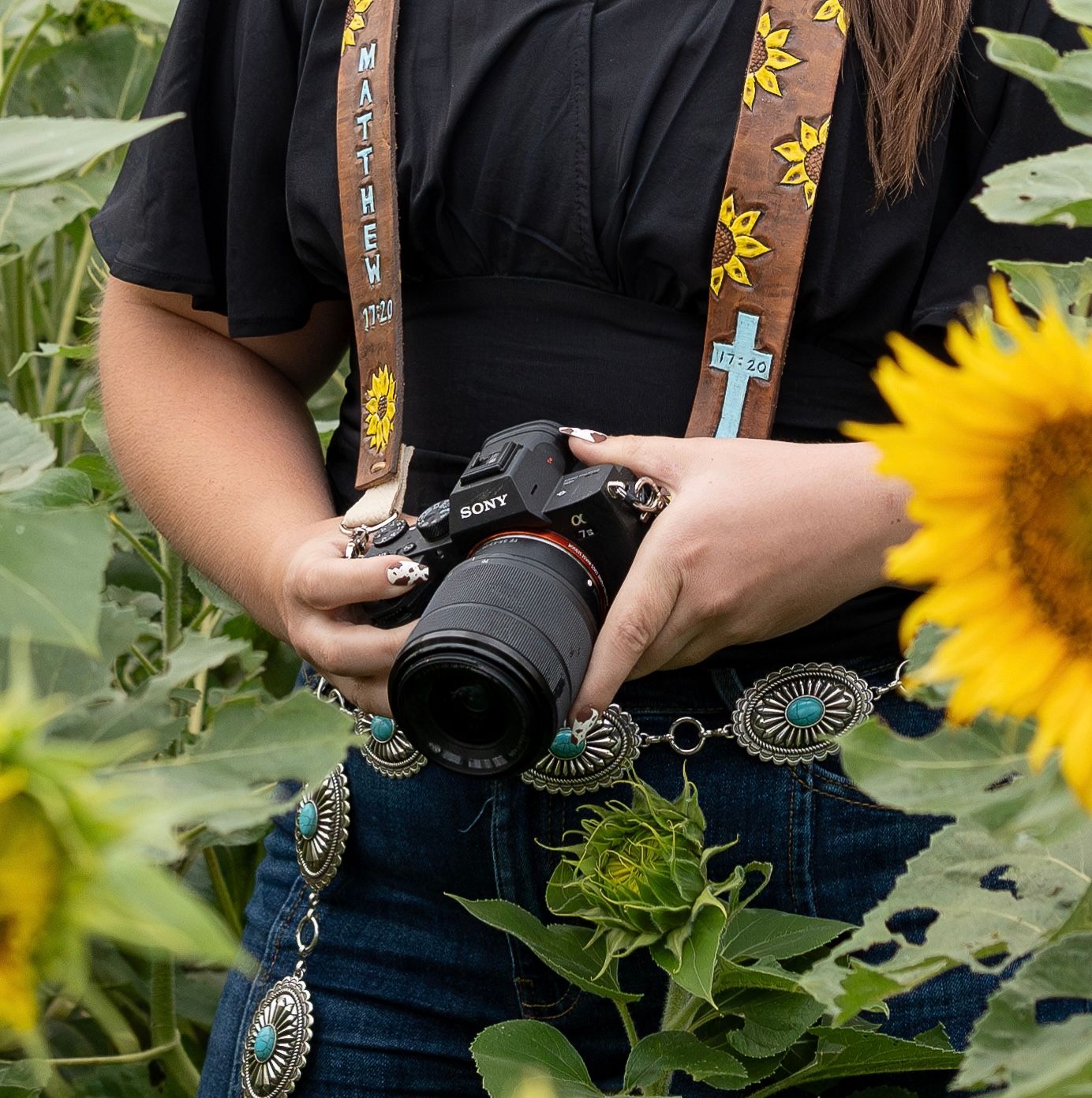 Photographer holding Sony camera with sunflower camera strap surrounded by sunflower field.