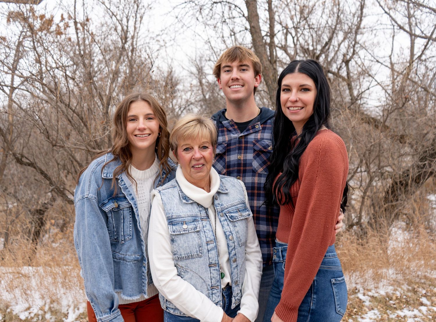 Woman with three young adults posing together outdoors in snowy winter landscape with bare trees.
