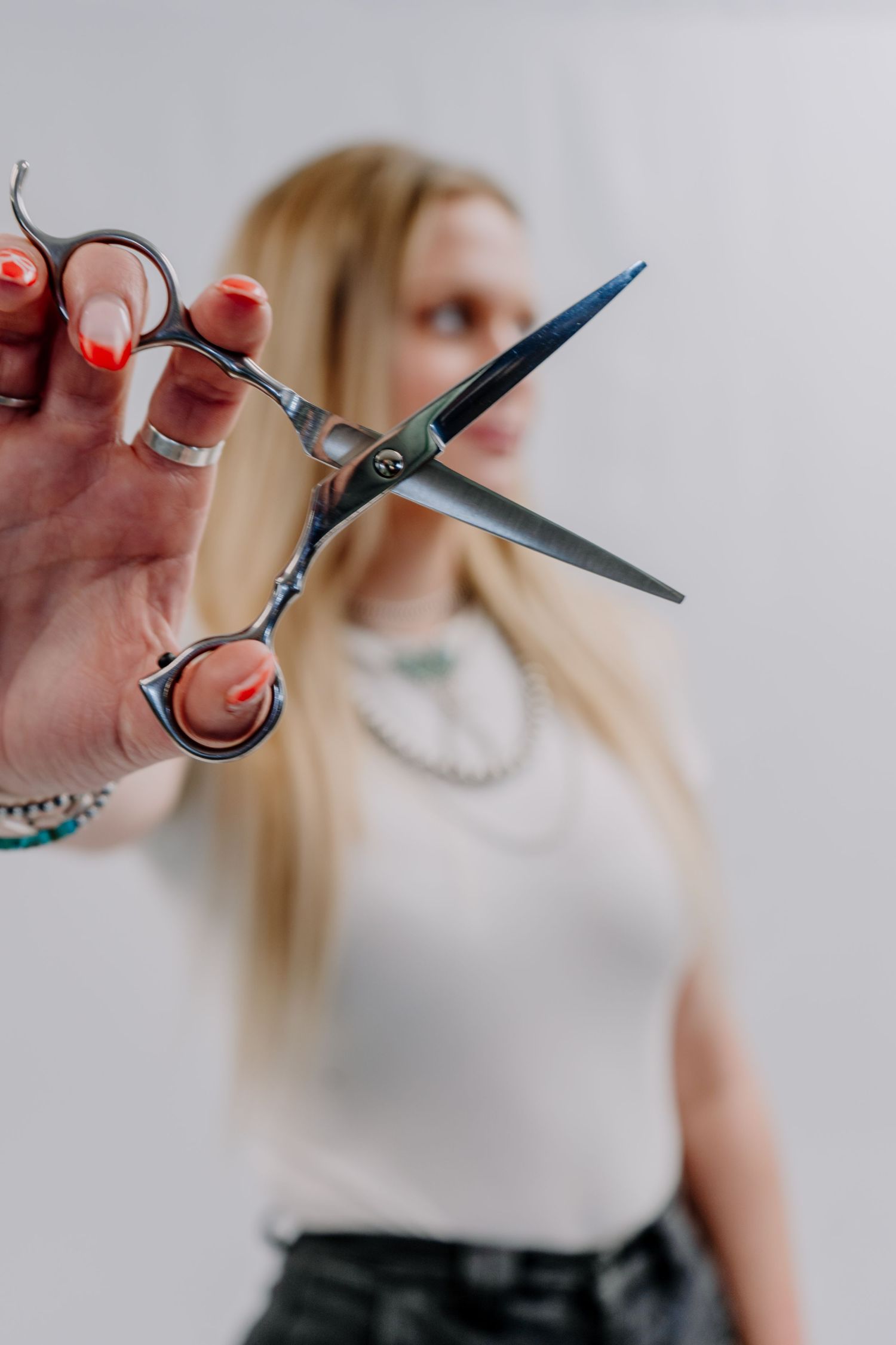 Close-up of professional hair cutting scissors held toward camera by blonde woman with red manicure.
