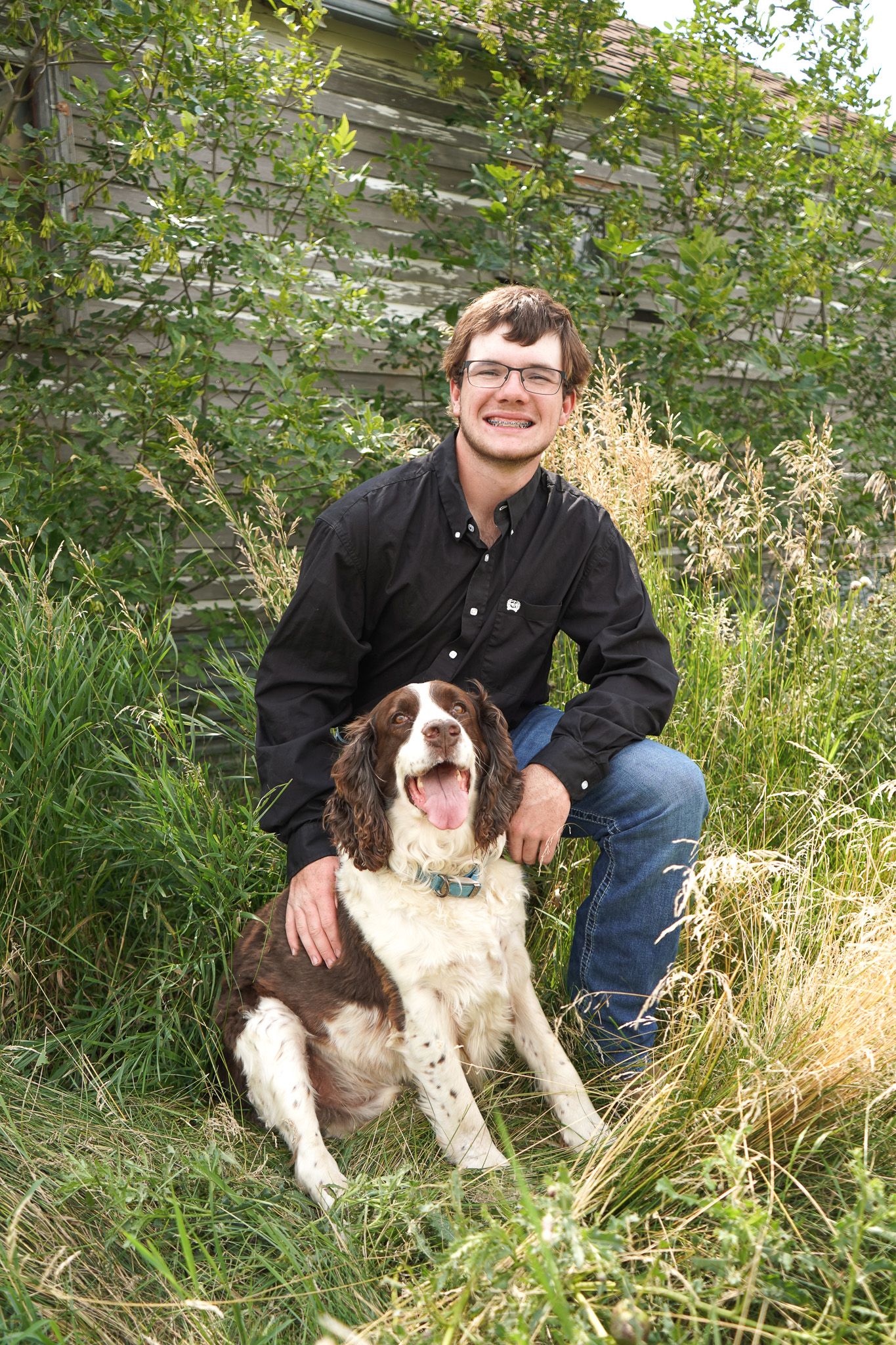Smiling young man in black shirt posing with brown and white Springer Spaniel outdoors.