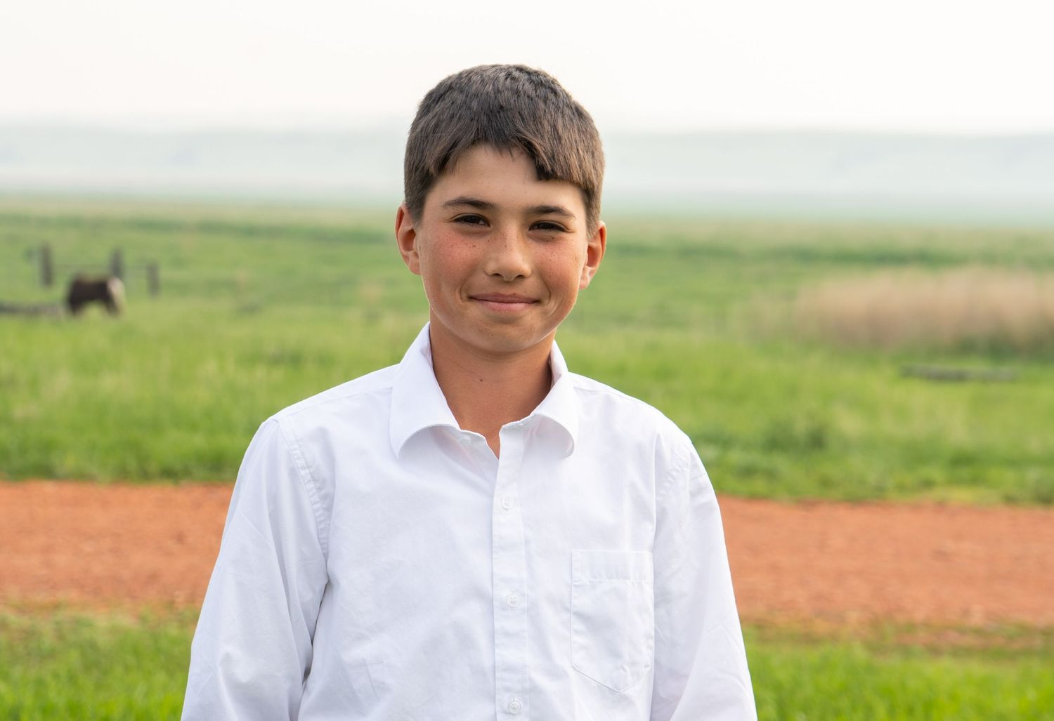 Smiling preteen boy in white dress shirt standing in a green field.