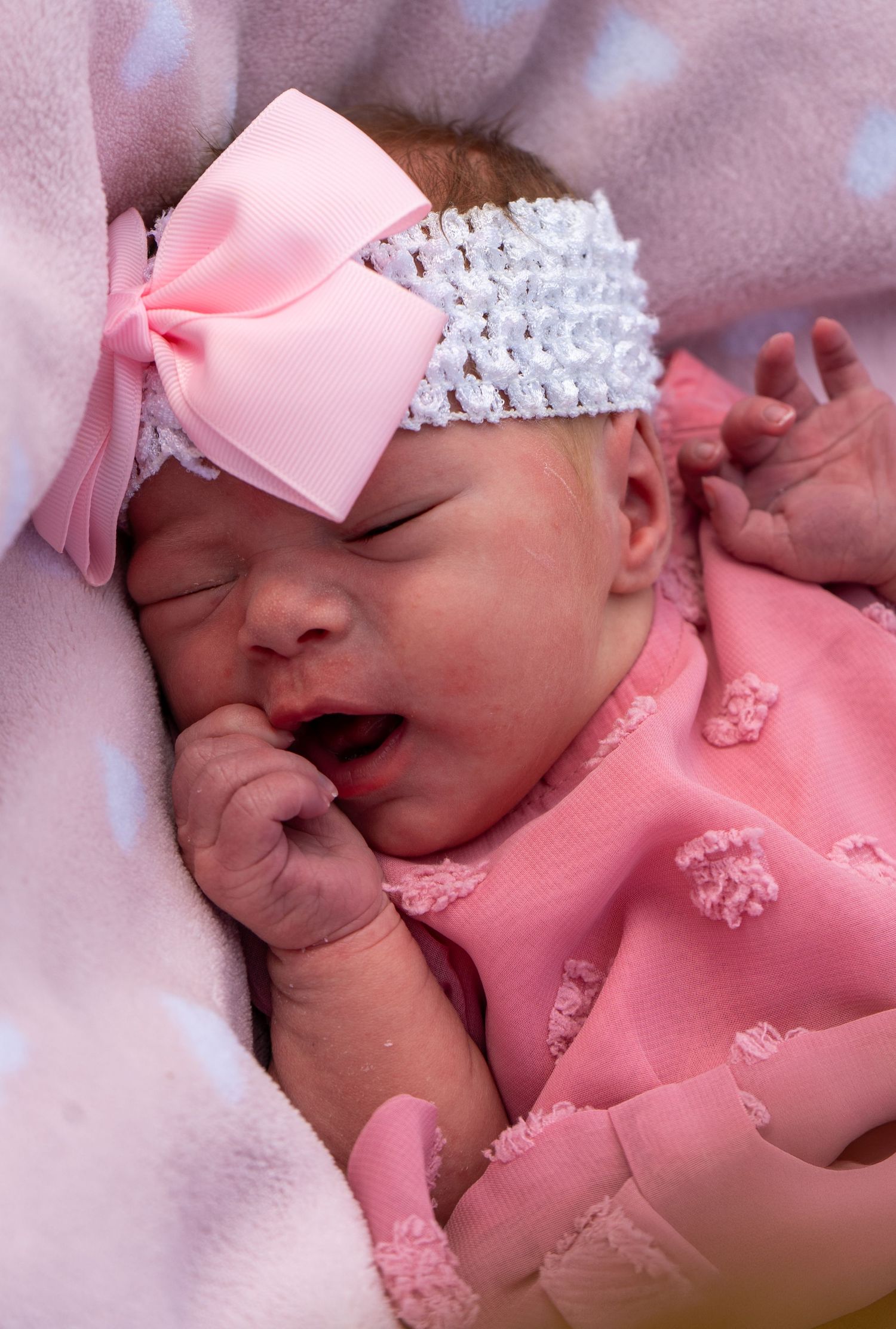Sleeping newborn baby girl in pink outfit with white bow headband.