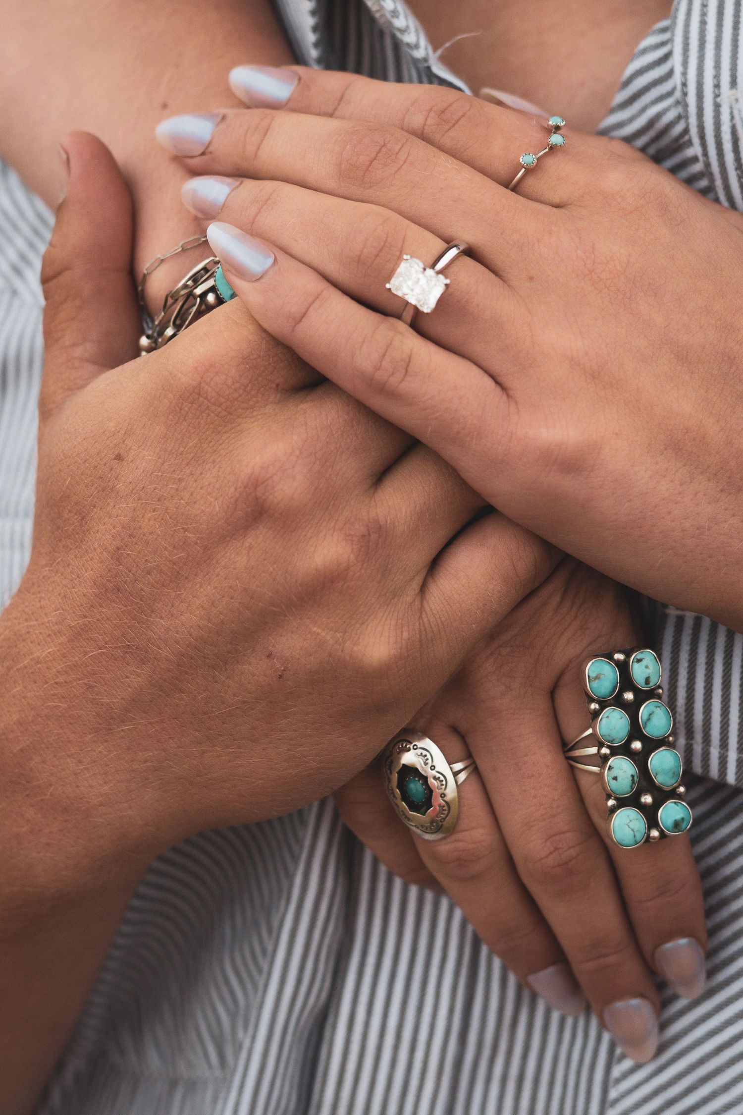 Close-up of two hands adorned with turquoise and silver rings including a square diamond engagement ring.