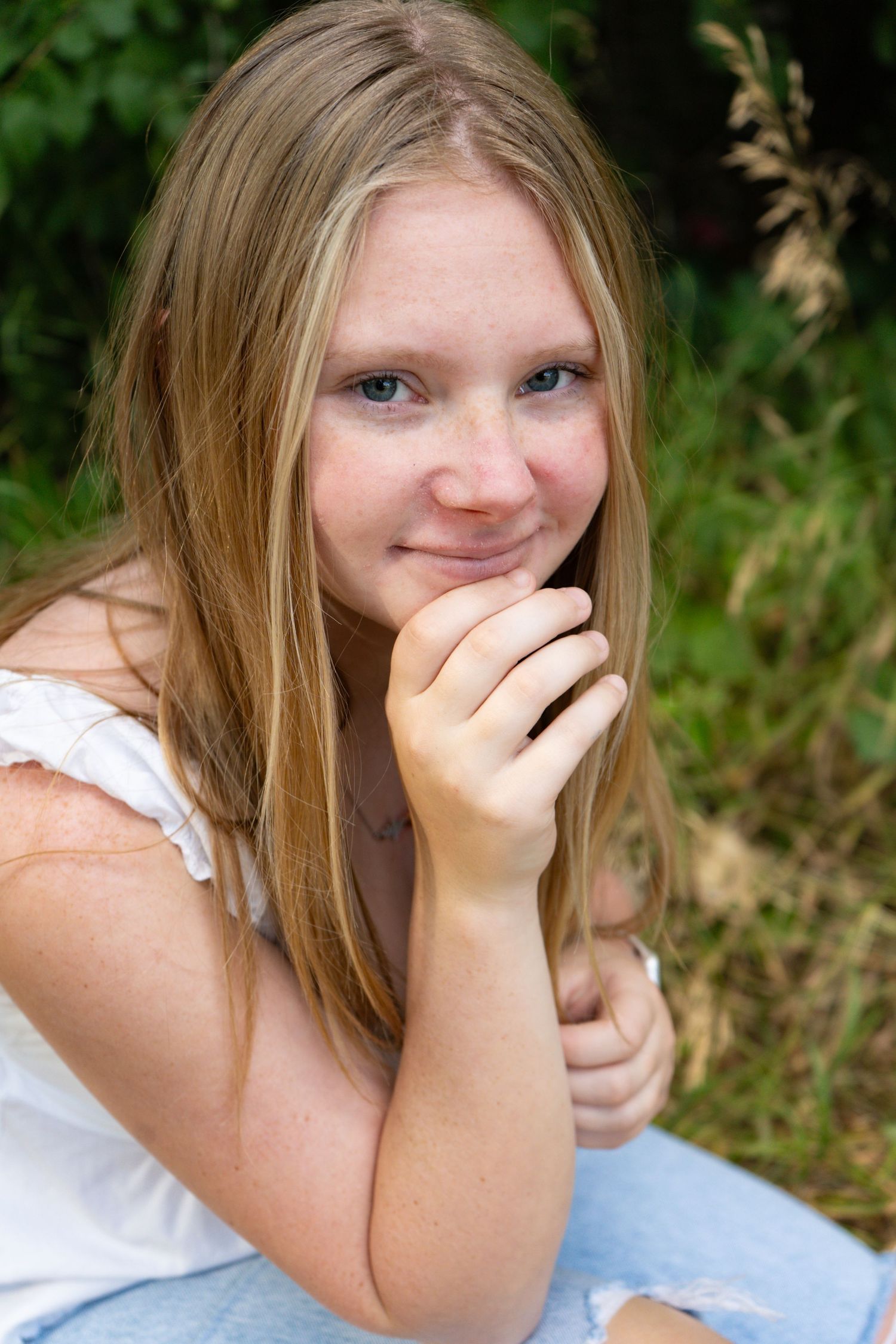 Close-up of a smiling blonde teen girl resting chin on hand in nature.