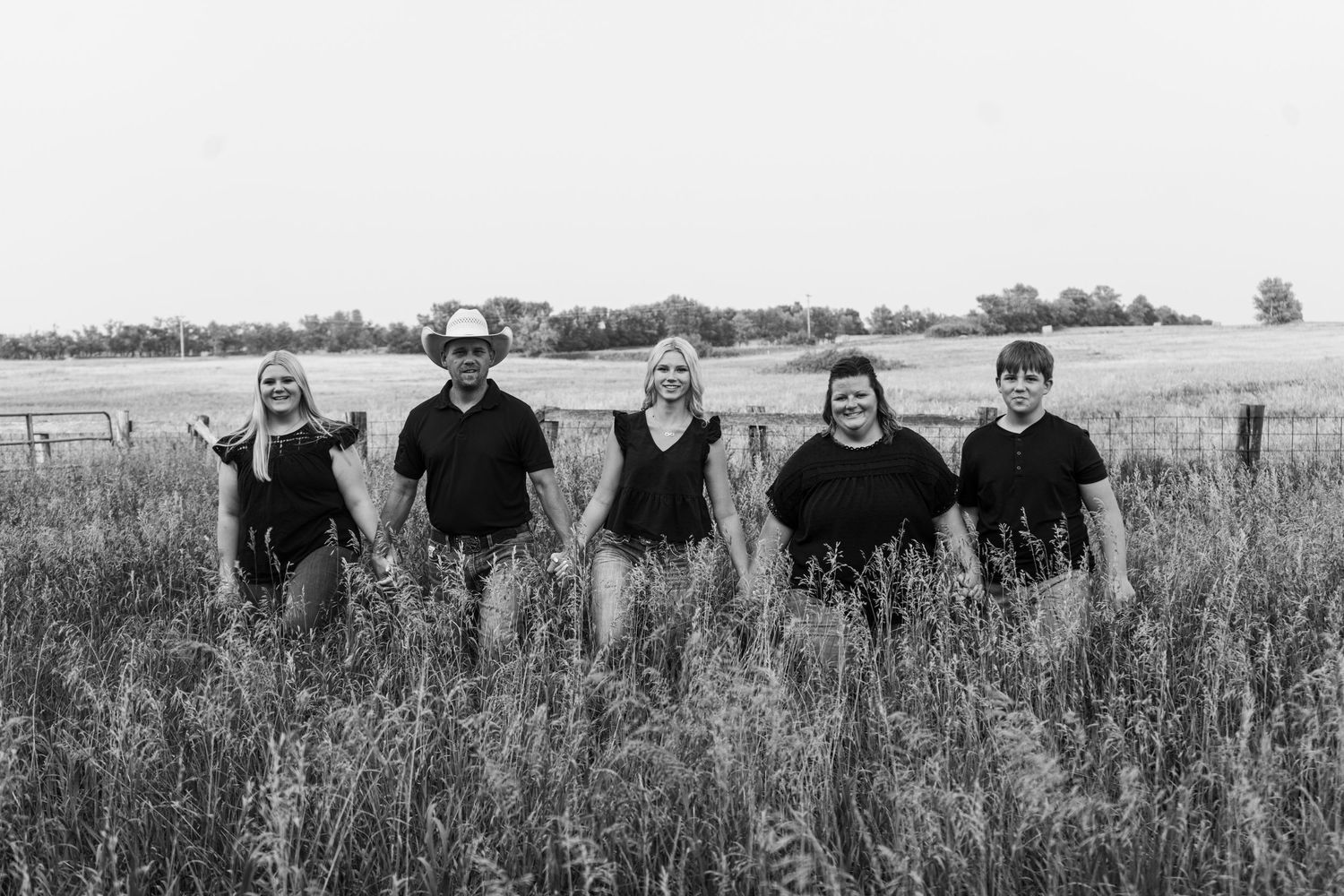 Black and white family portrait of five people standing in tall grass field.