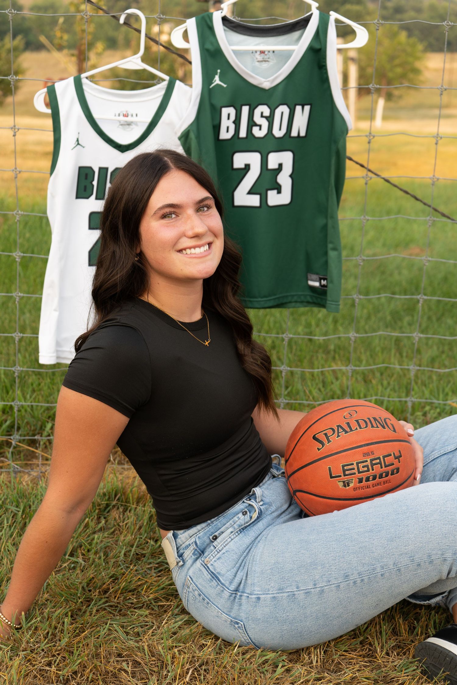 Young female athlete poses with Spalding basketball in front of Bison jersey number 23 on fence.