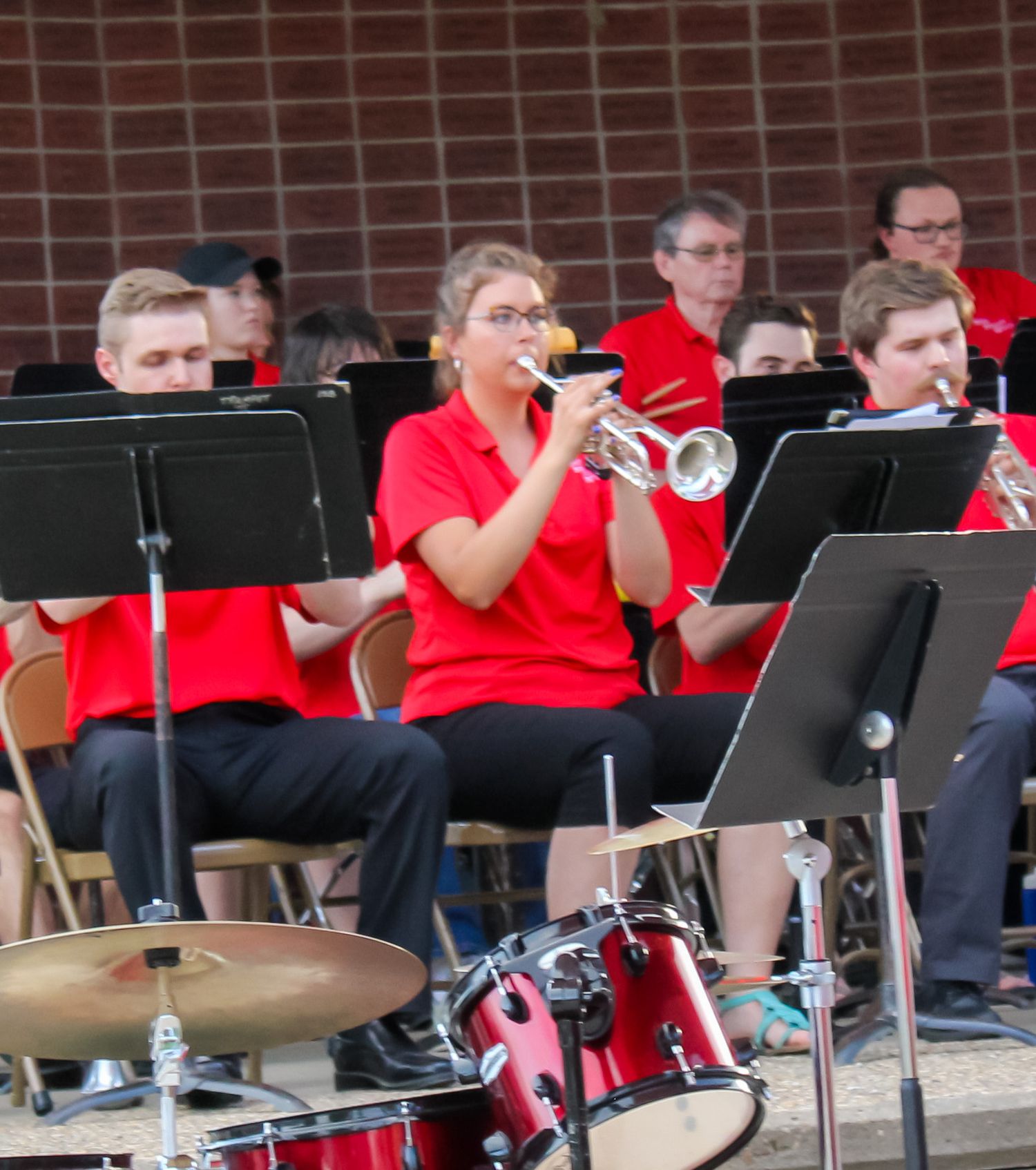 Female musician playing trumpet in red uniform at an outdoor band shell concert performance.