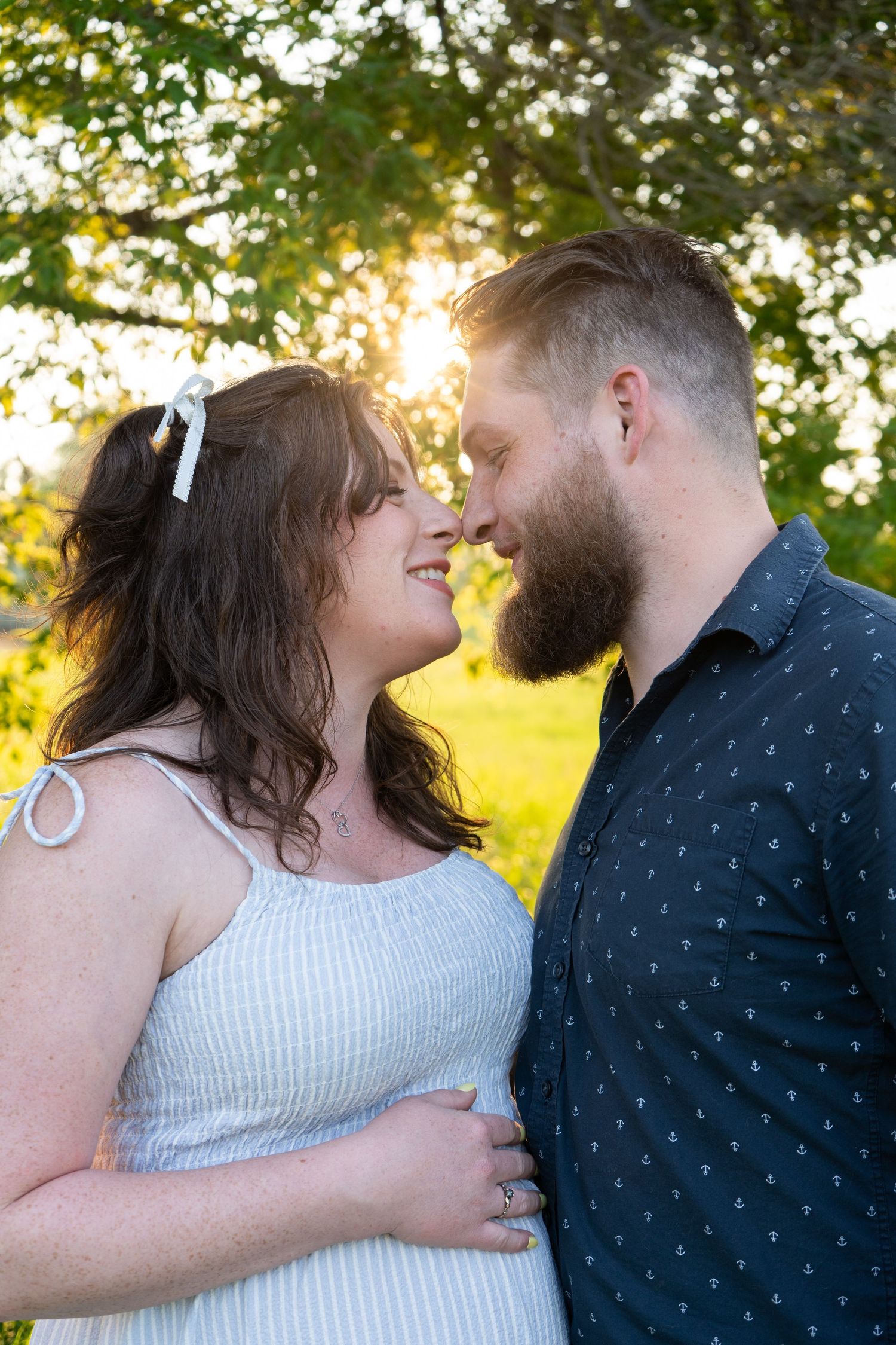 Couple sharing a romantic nose-to-nose moment at golden sunset in lush green outdoor setting.