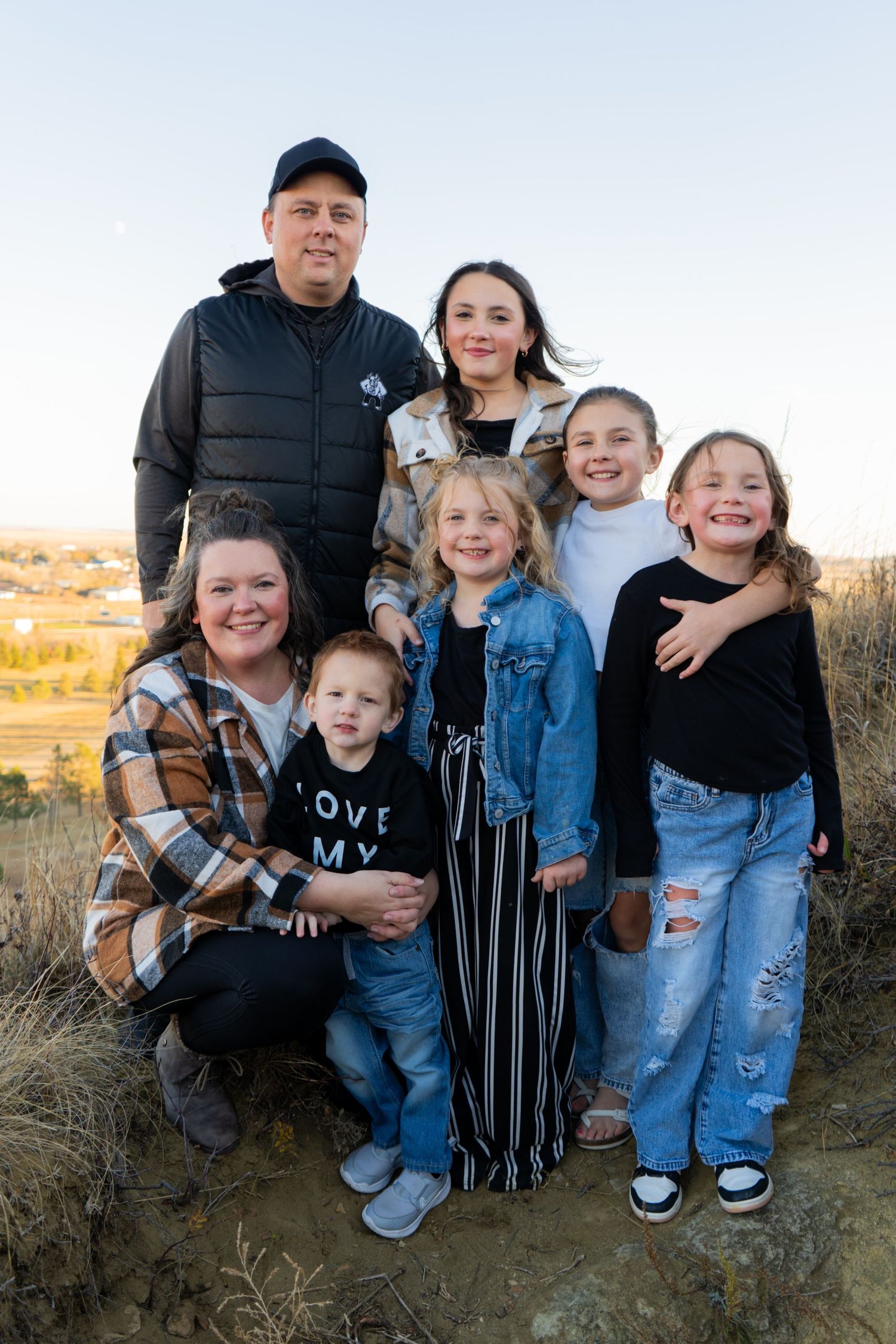 Happy family of seven posing together outdoors on a hillside during golden hour.