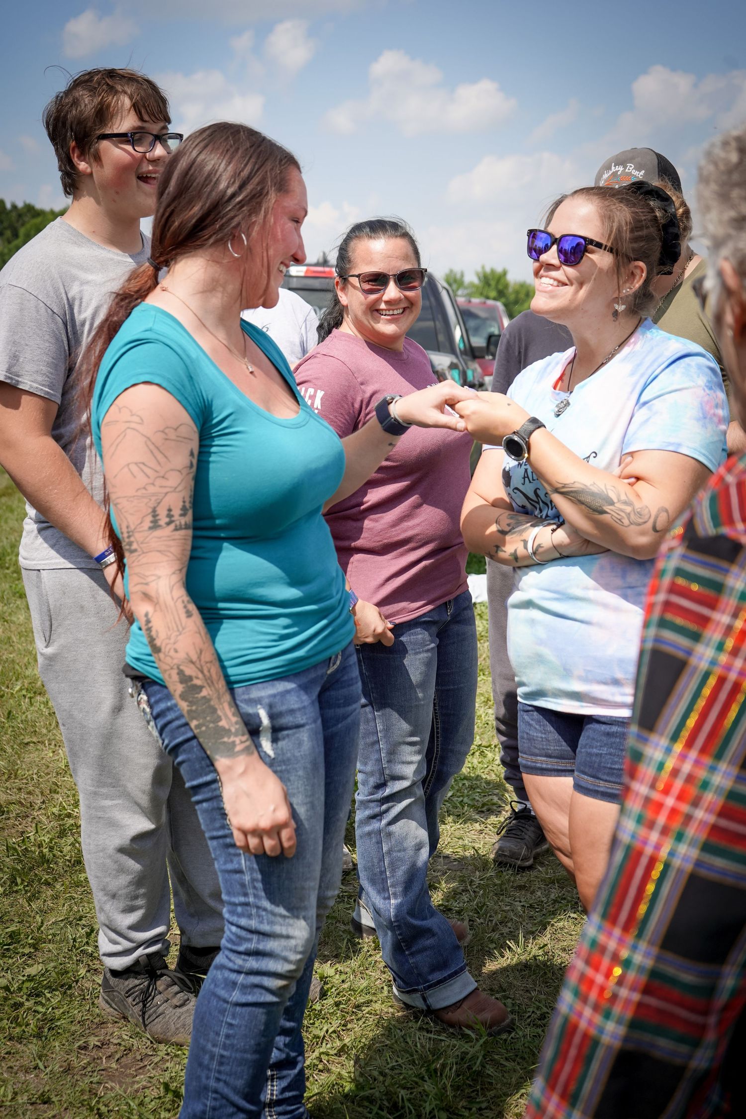 Group of women laughing and admiring engagement ring at outdoor celebration.