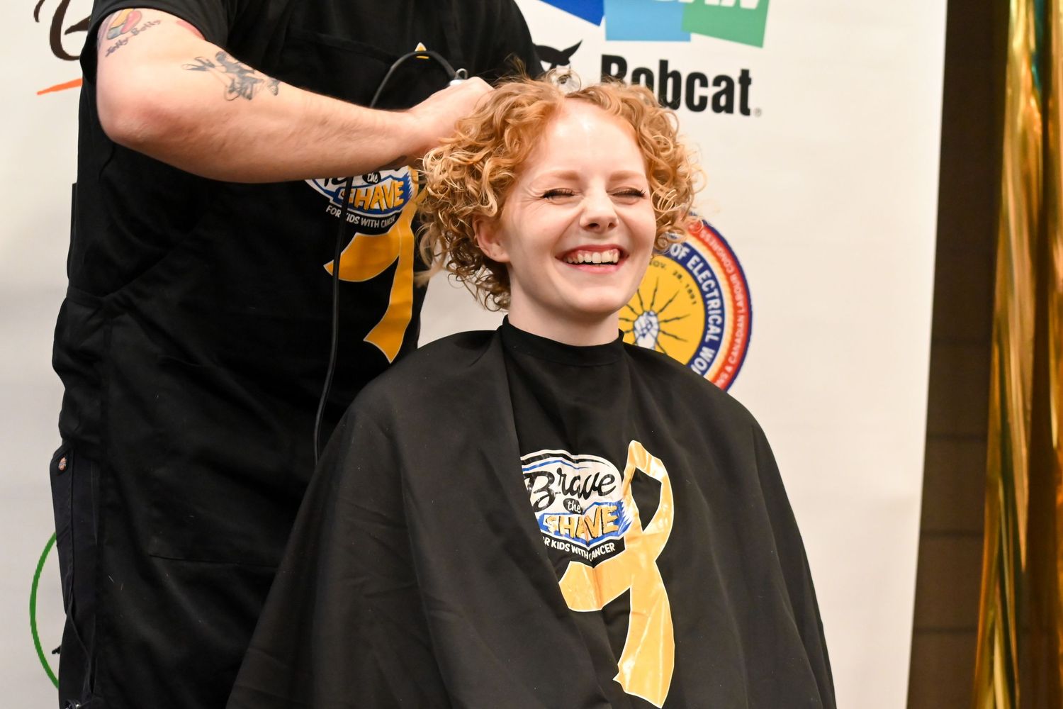 Smiling redhead woman getting her head shaved at a Brave the Shave charity fundraising event.