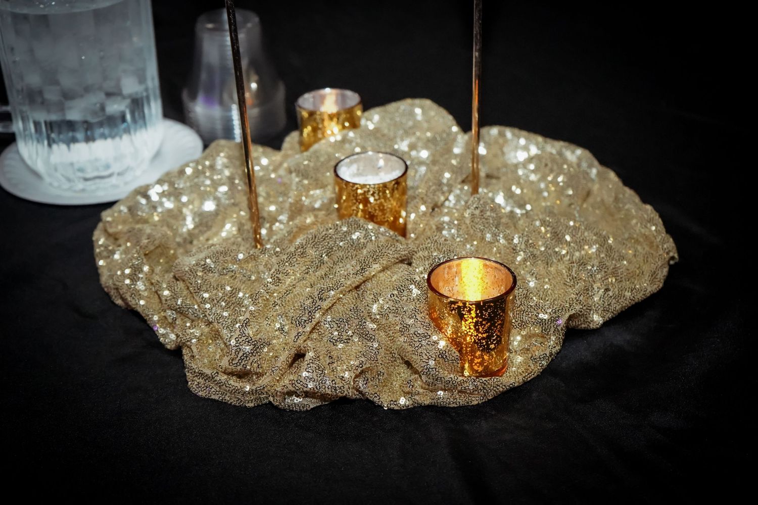 Gold glitter centerpiece with votive candles and tall taper candles on black tablecloth at formal event.