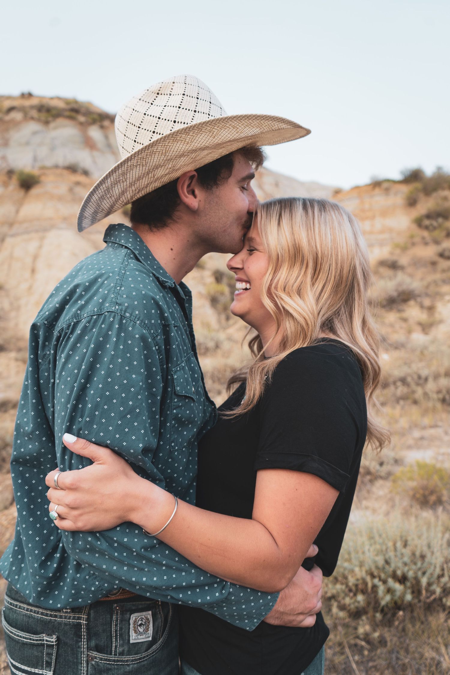 A couple in a western desert setting shares a romantic moment, nearly kissing while embracing.