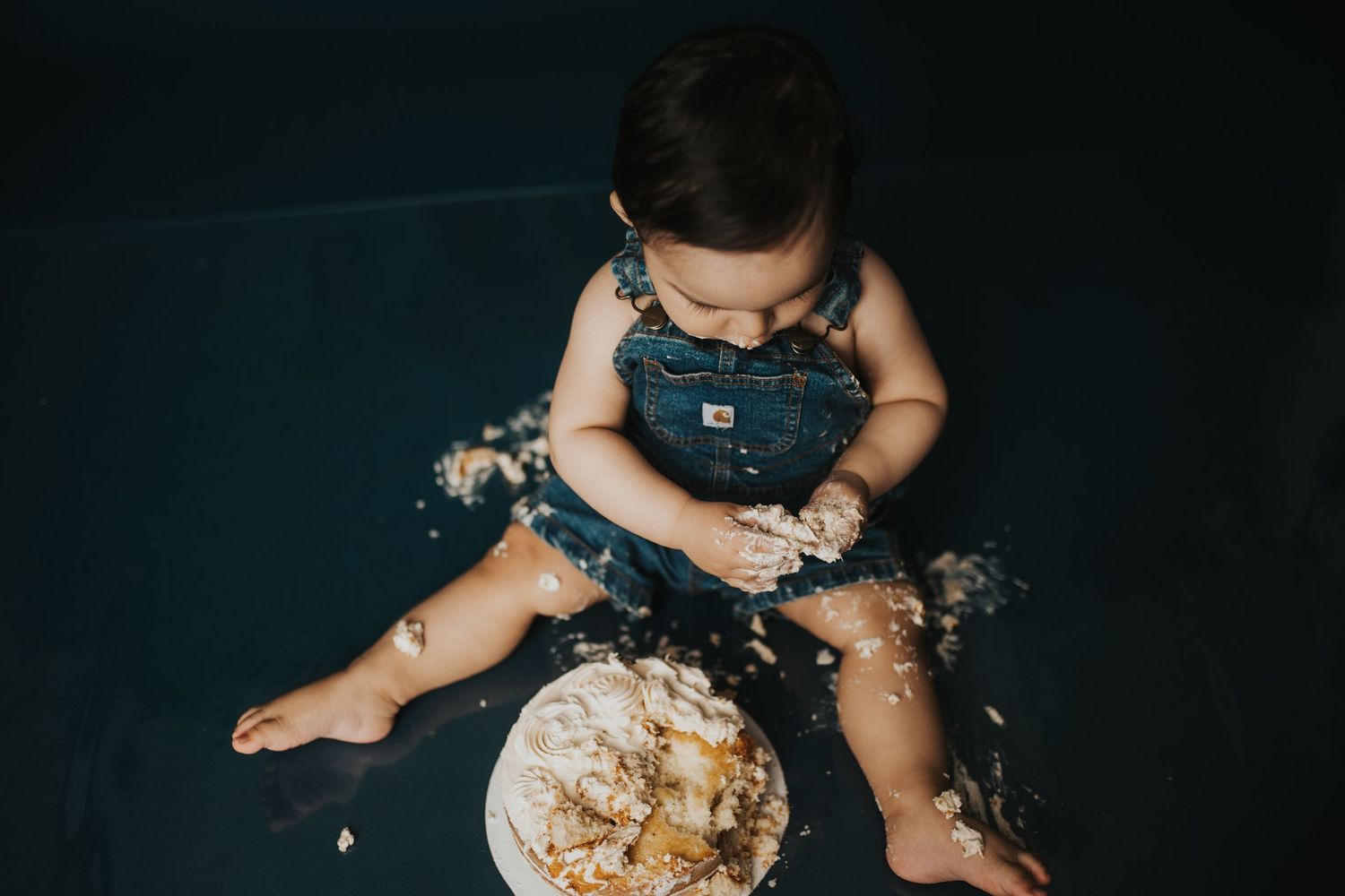 Messy cake smash scene with scattered frosting against dark background.