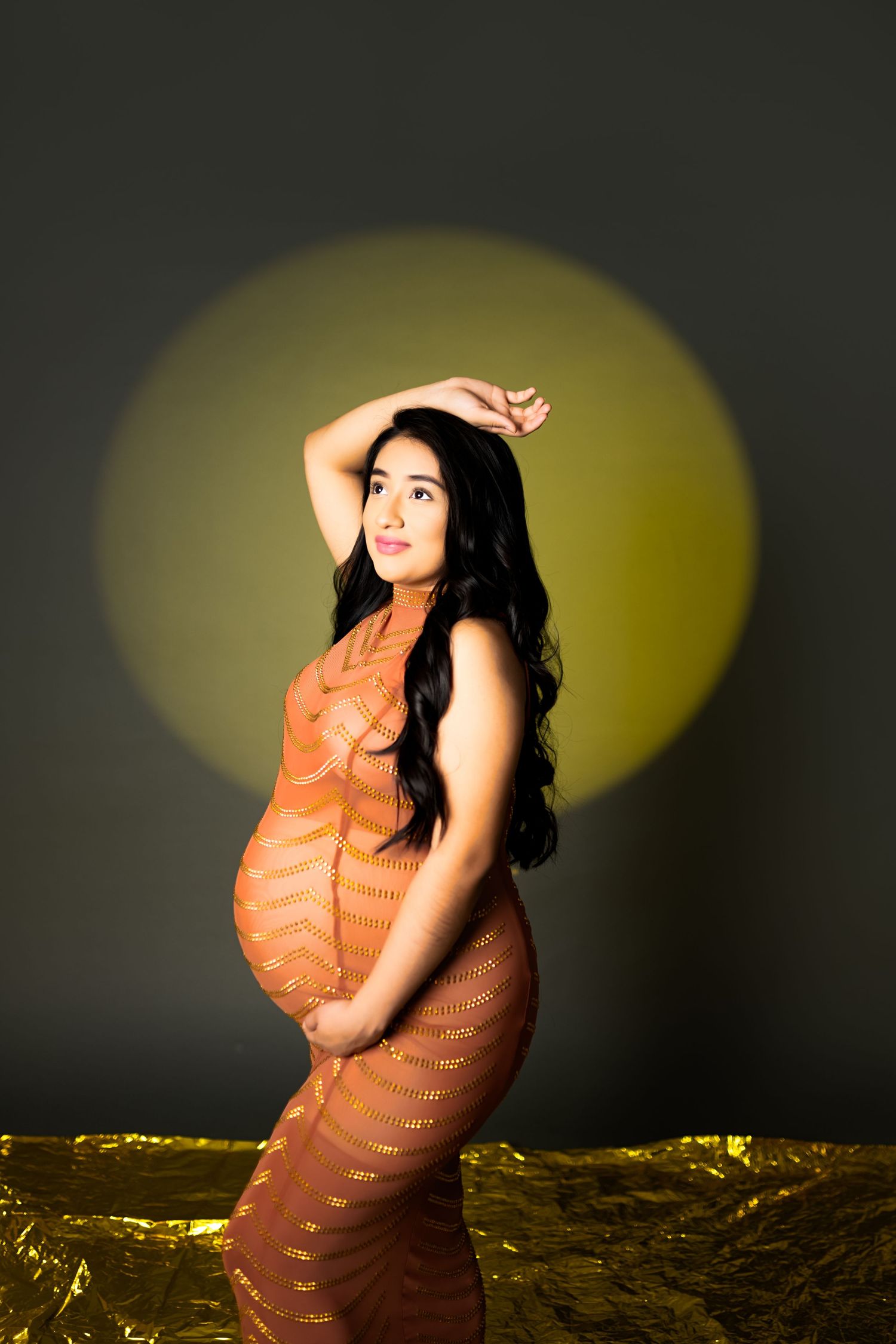 Artistic maternity portrait with golden circle backdrop and orange dress.