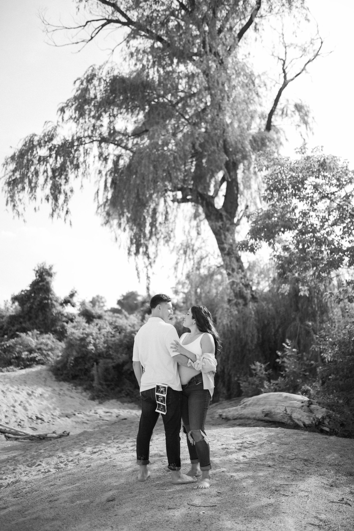 Couple standing close together under willow tree in black and white photograph.
