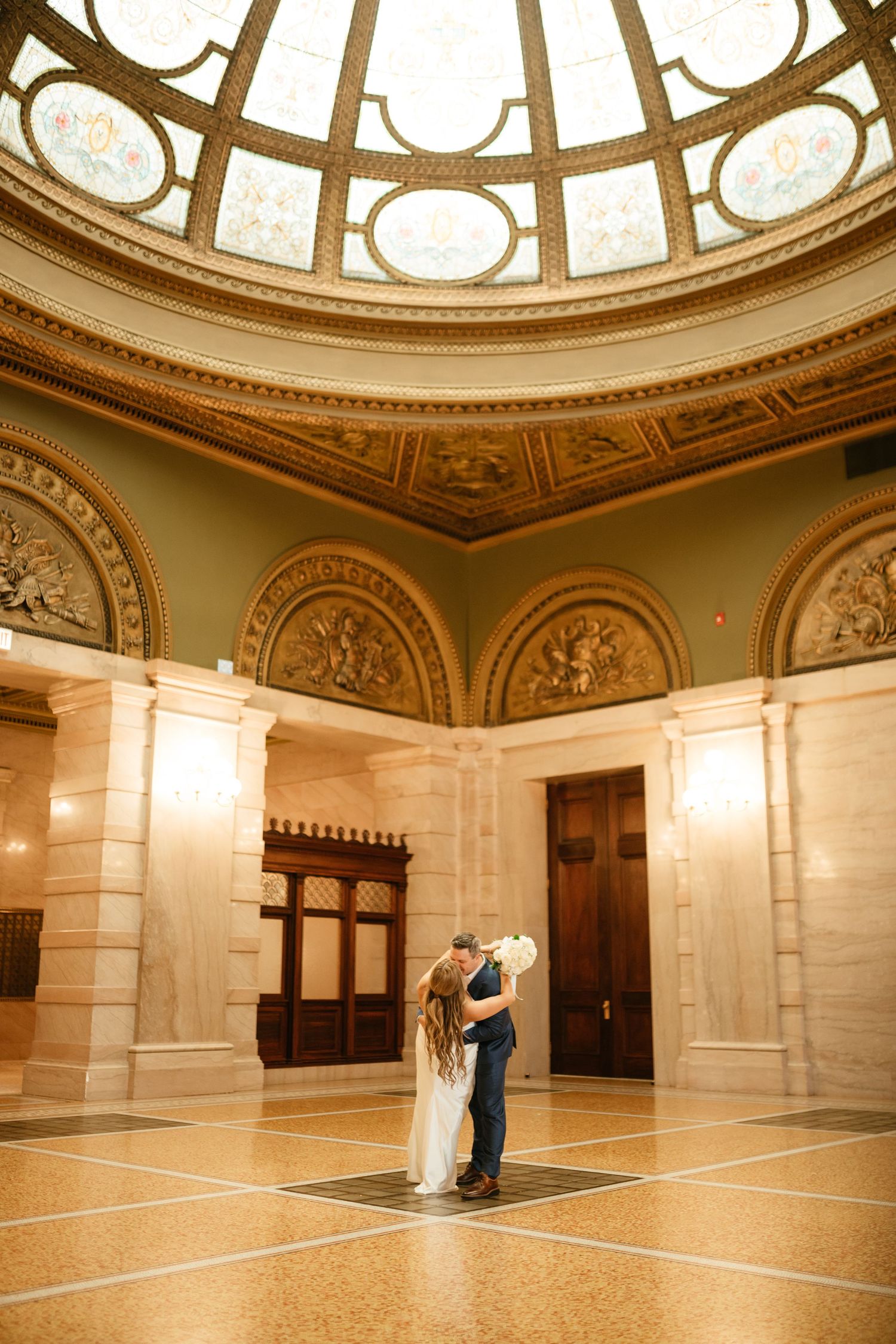 Elegant ballroom with ornate domed ceiling and marble floors in warm sepia tones.
