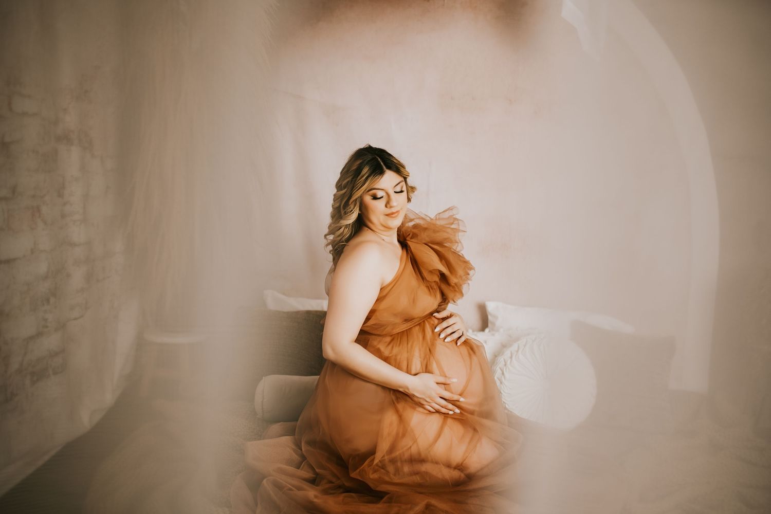 Artistic maternity boudoir photos with soft sepia tones and flowing fabric.