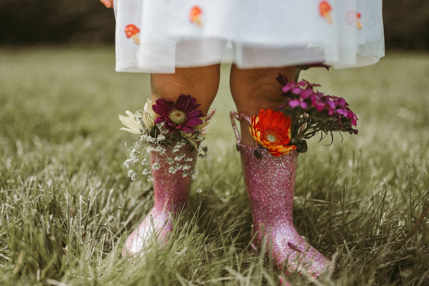 Pink glitter boots with floral arrangements standing in grass.