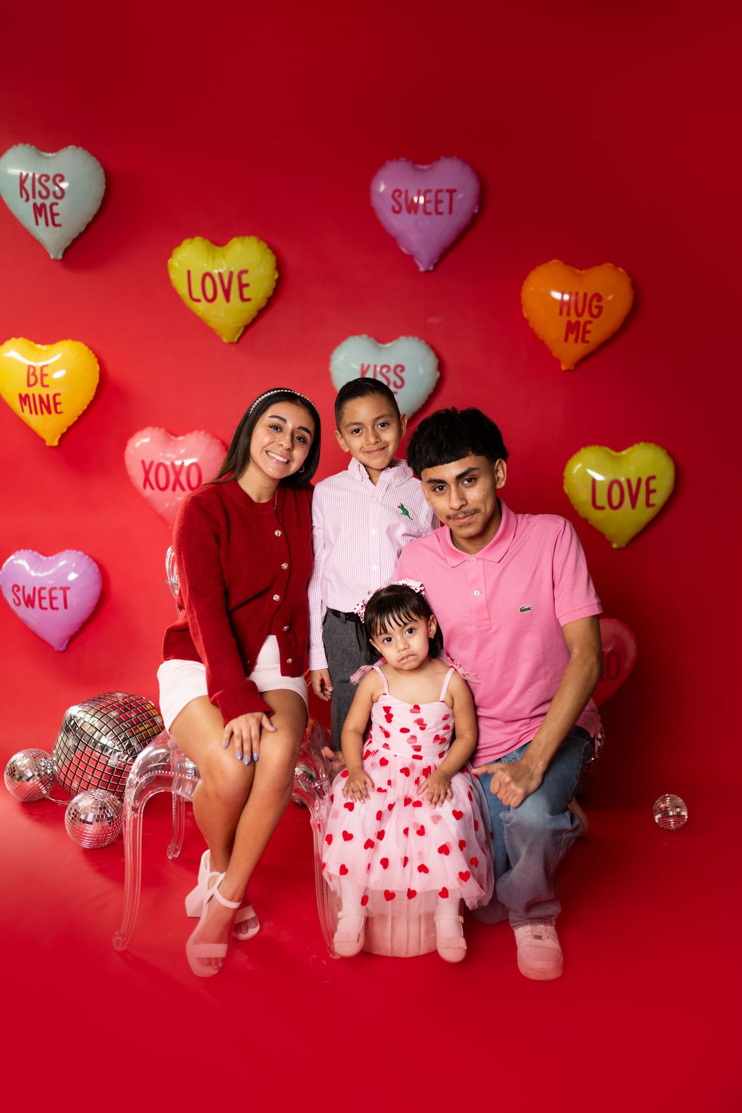 Valentine's themed photo with heart balloons against red background in matching pink outfits.