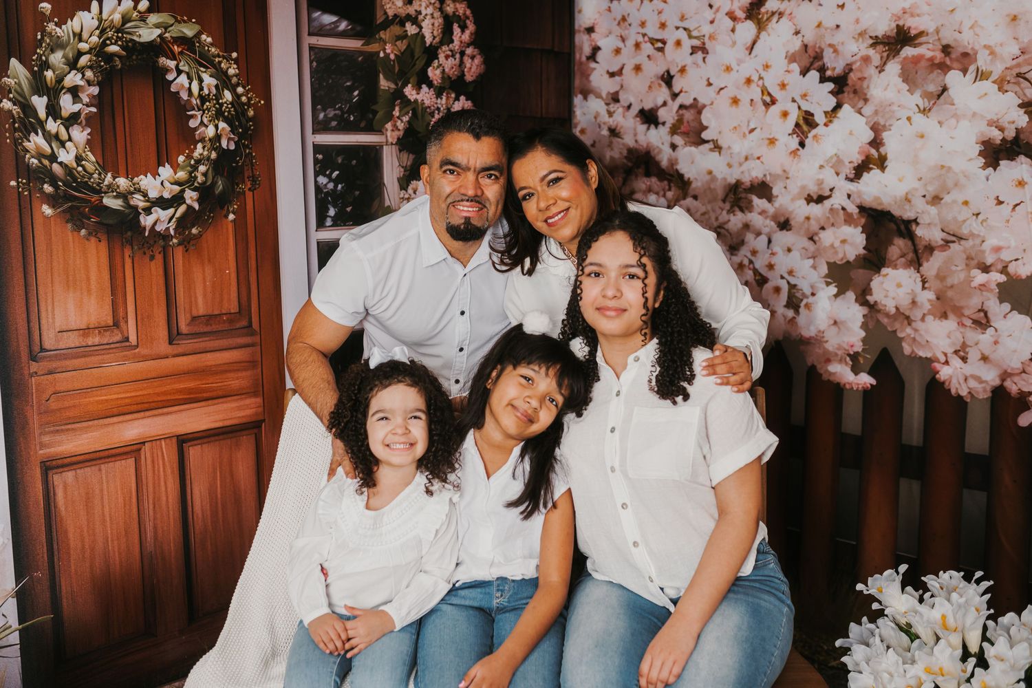 Family portrait session under blooming cherry blossom trees with rustic wooden door background.