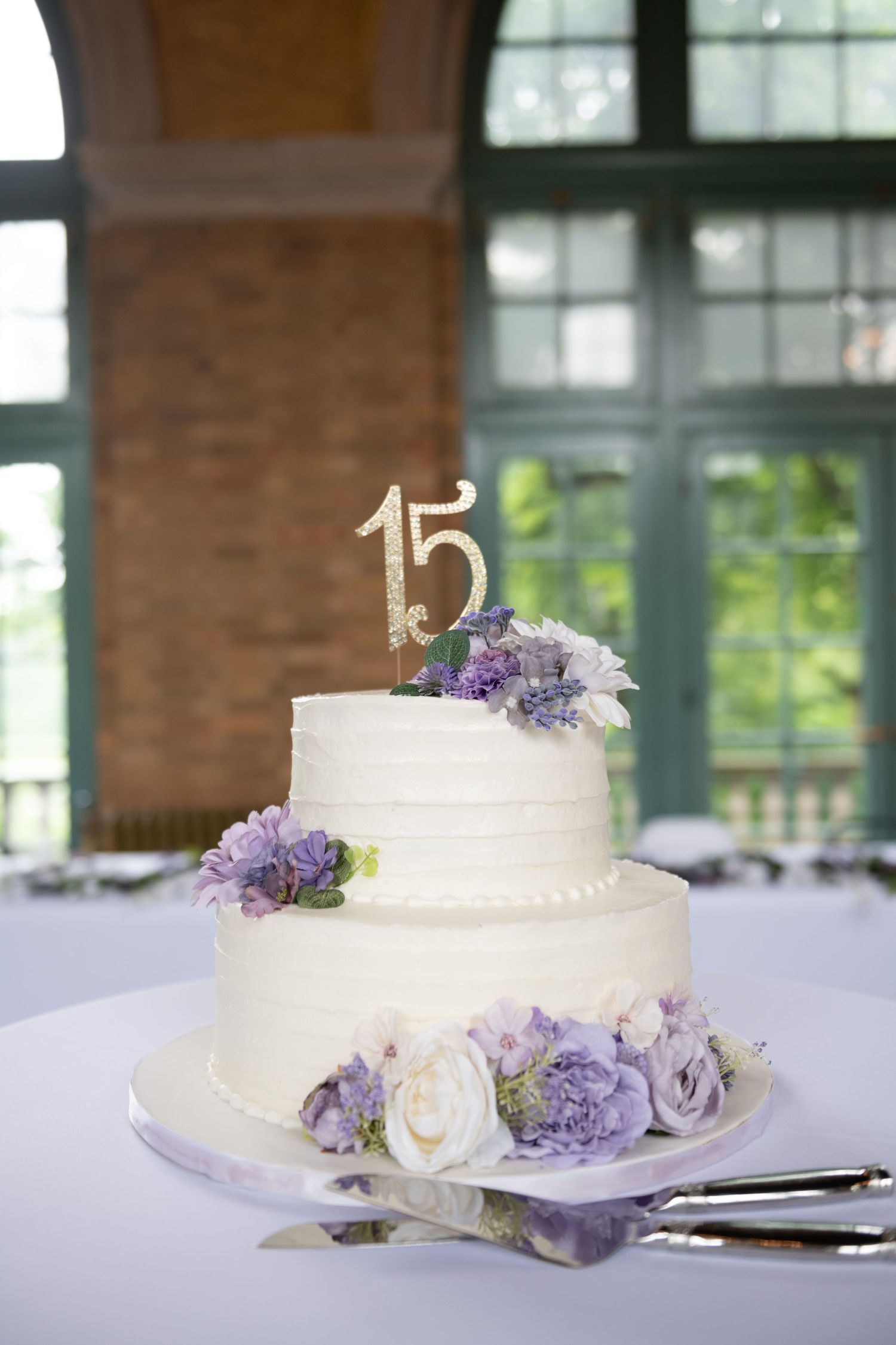 White wedding cake decorated with purple and lavender flowers on display at reception.