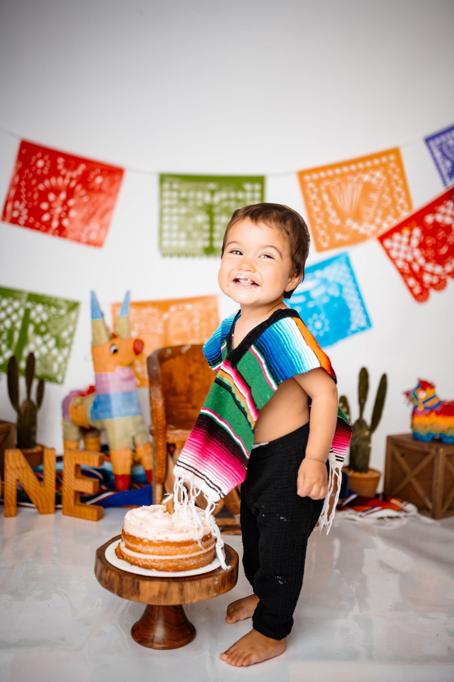 A festive cake smash scene with bright Mexican-style paper decorations and wooden accents.