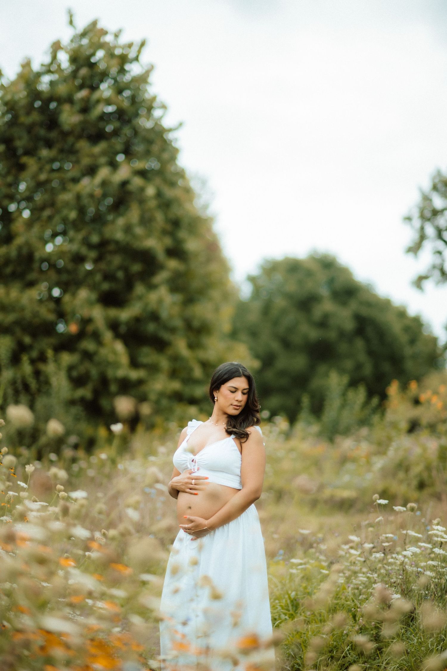 Dreamy outdoor maternity photo in field of white wildflowers.