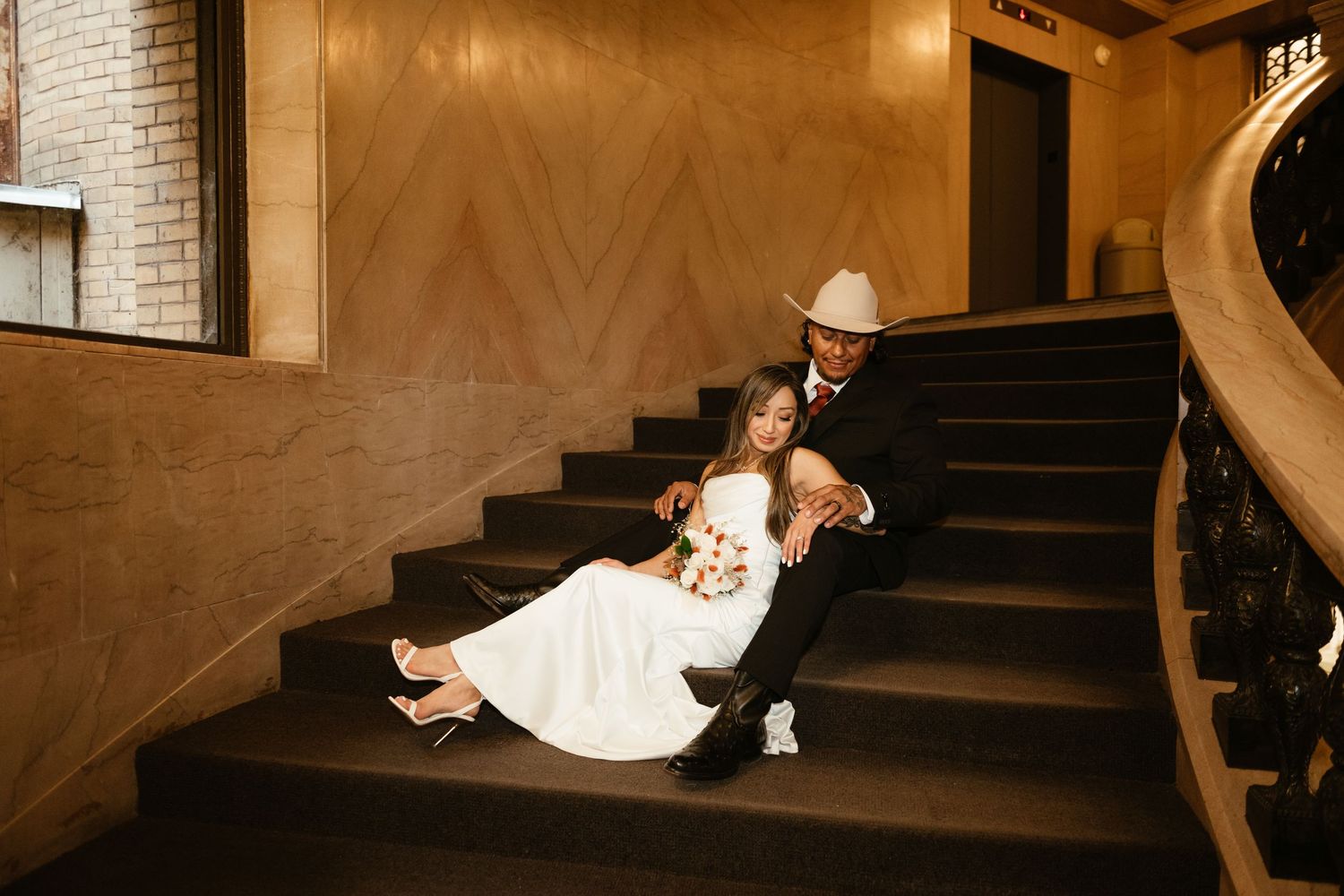 A couple poses on vintage brick stairs in an elegant indoor setting.