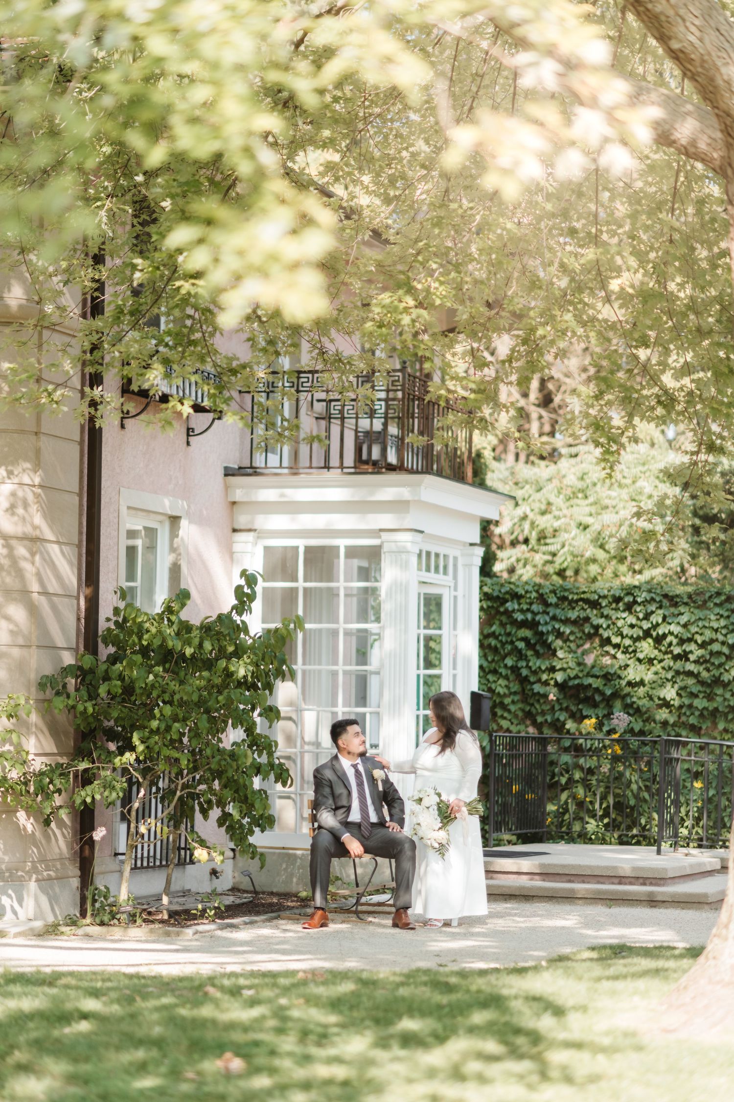 Elegant wedding photos taken in a lush garden setting with white building and iron fence details.