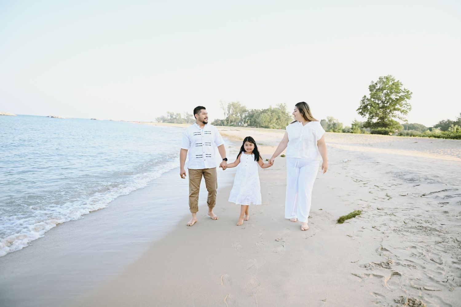A family walking together along a beach shoreline on a sunny day.