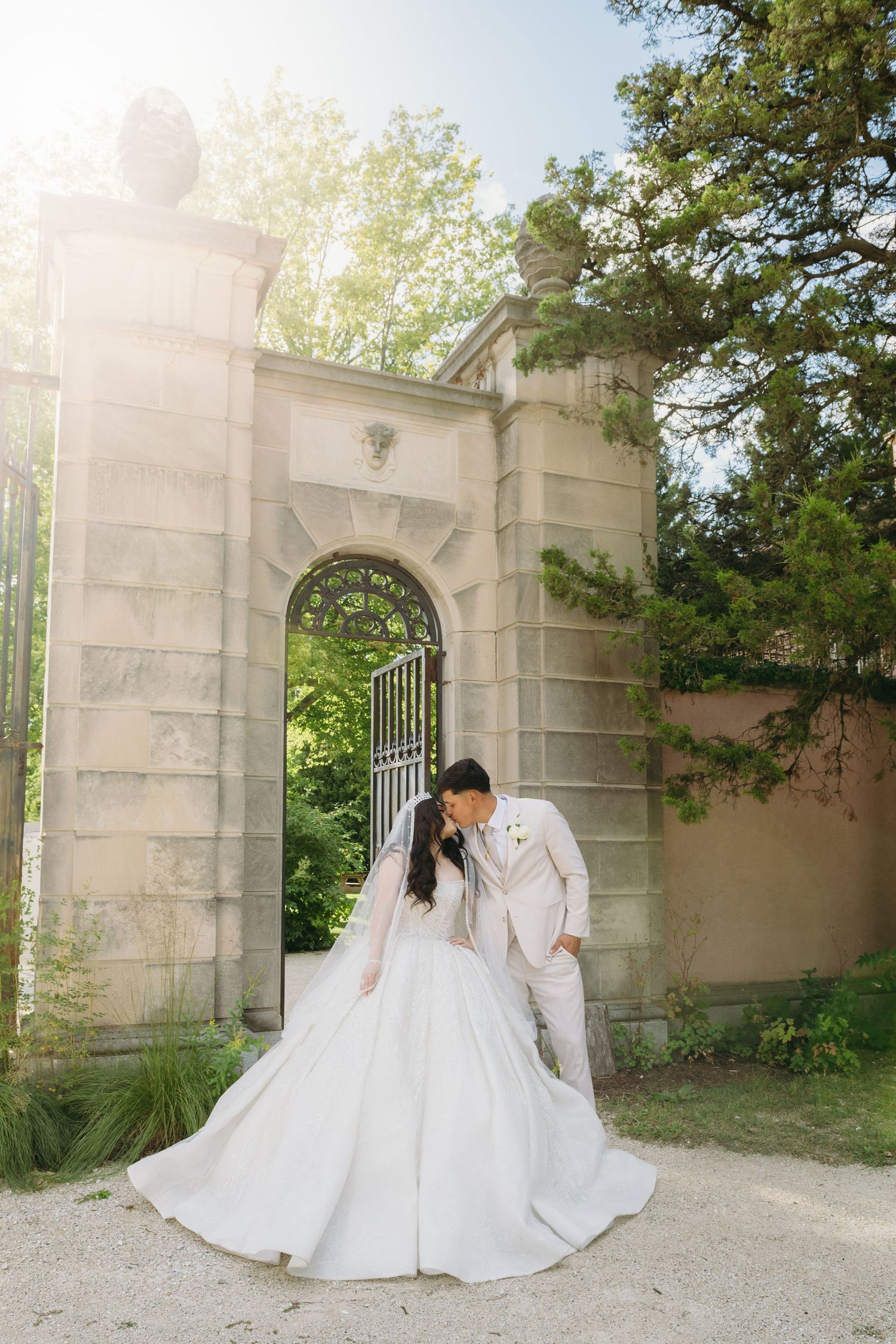 Wedding couple posing by elegant stone archway and gates in garden setting.