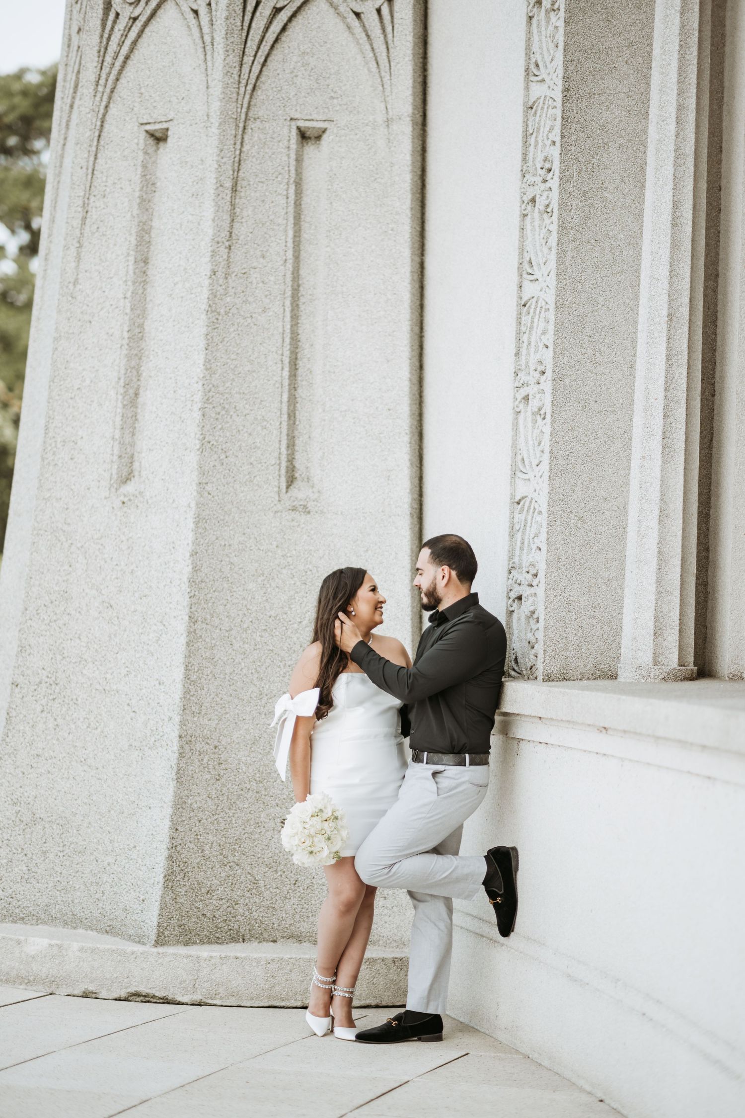 A romantic couple shares intimate moments between white stone columns in an elegant architectural setting.