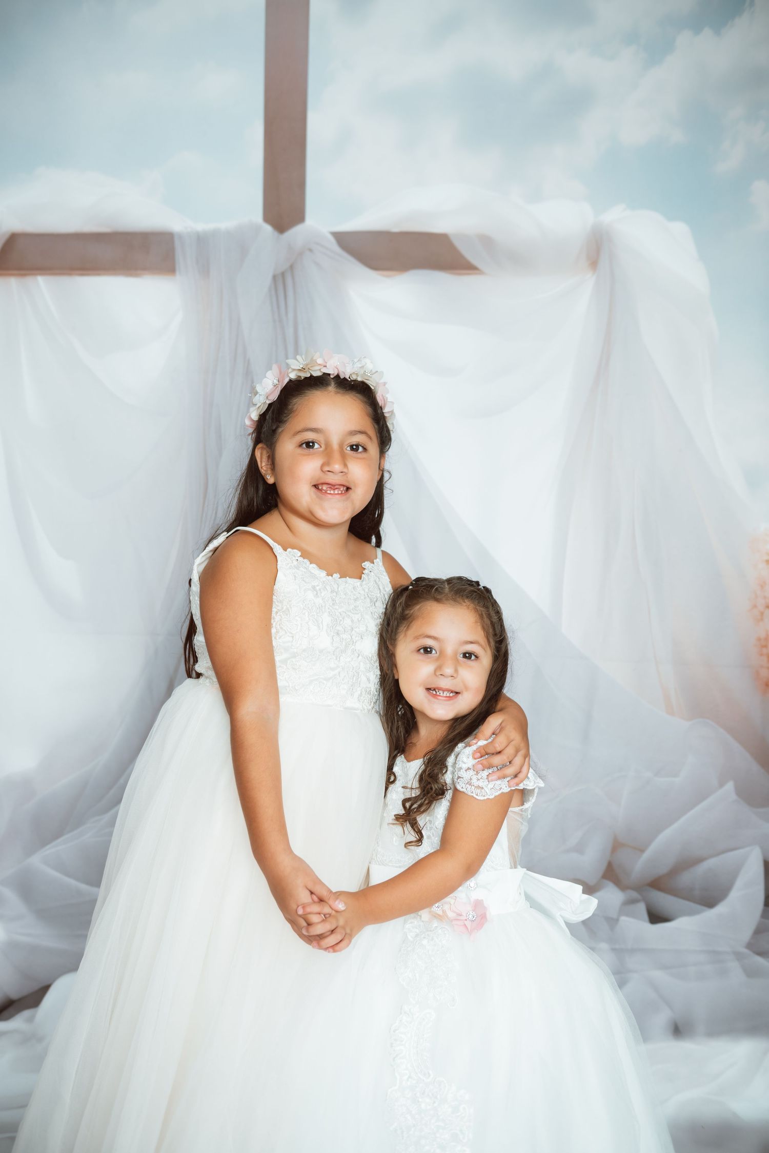 Two children in flowing white dresses posing together against light airy backdrop.