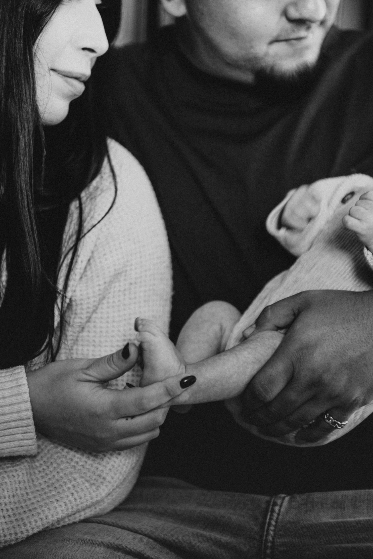 Black and white photo of a couple tenderly holding their newborn baby's tiny hand together.